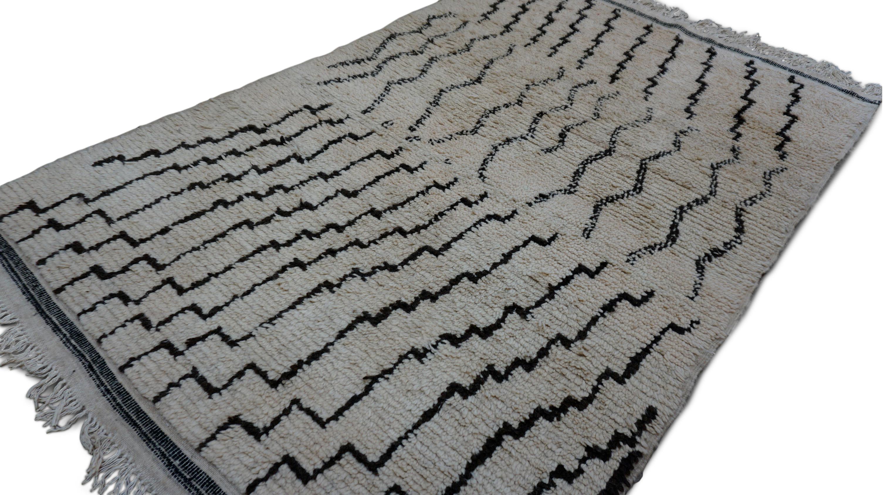 This hand-knotted wool rug showcases a minimalist Beni Ourain aesthetic elevated by bold, contrasting linework. The rug features a unique composition of staggered black zigzag lines alternating with wavy, freeform motifs across a warm ivory