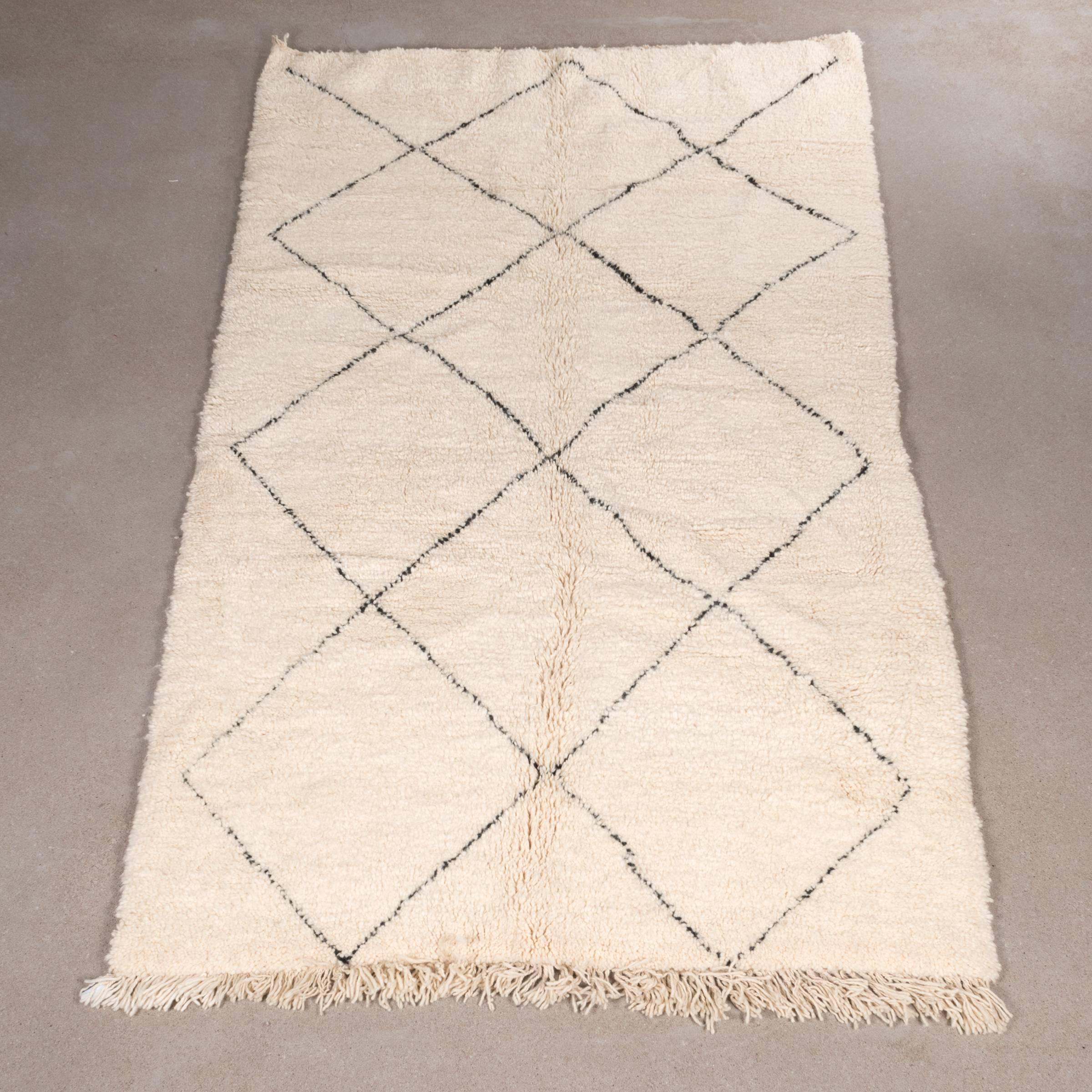 This vintage Beni Ourain rug is carefully selected in Morocco and has a soft ivory color due to the wool's natural color and are accompanied by dark grey stripes. The rugs are named after the Berber village 'Beni Ourain' in the mid-atlas mountain