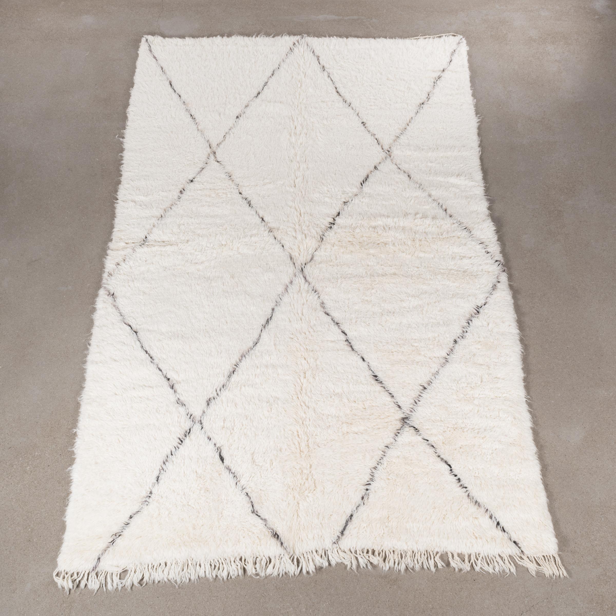 This vintage Beni Ourain rug is personally selected in Morocco and has a soft ivory color due to the wool's natural color and are accompanied by dark grey stripes. The rugs are named after the Berber village 'Beni Ourain' in the mid-Atlas mountain