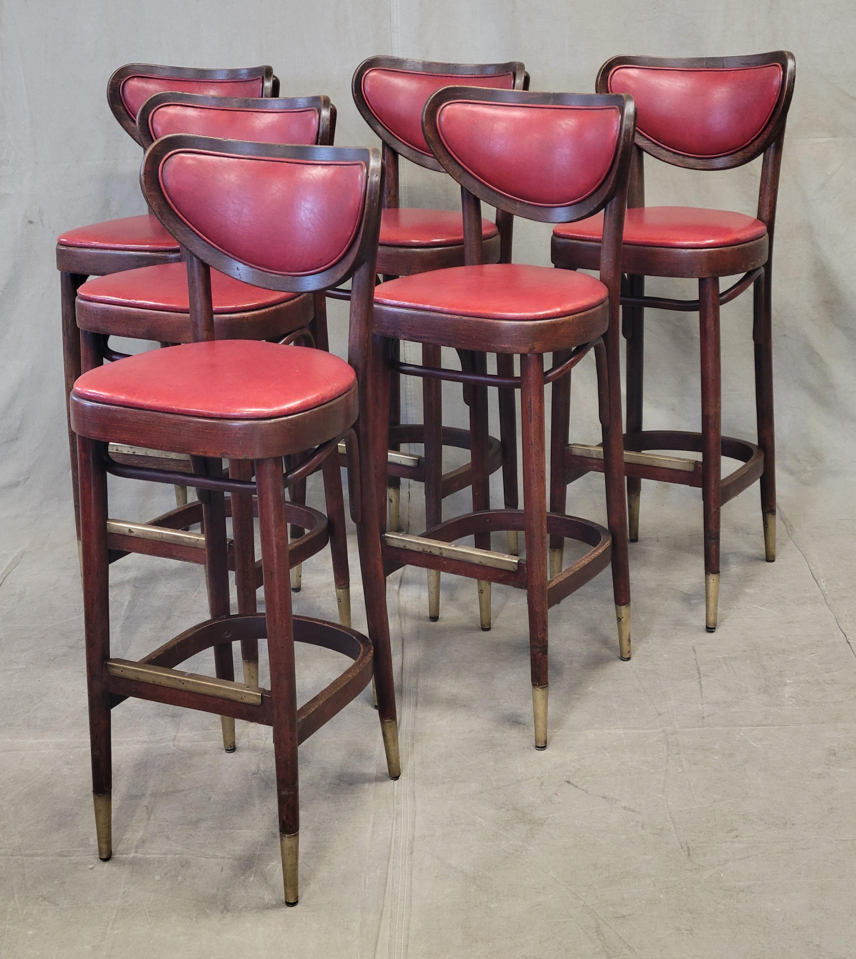 A classic set of 6 vintage 1930s bentwood bar stools with original red vinyl upholstery and brass feet and footrest. Stools are sturdy and ready to be used. Wood is a rich mahogany brown tone. Old red vinyl is high quality and has great worn patina.