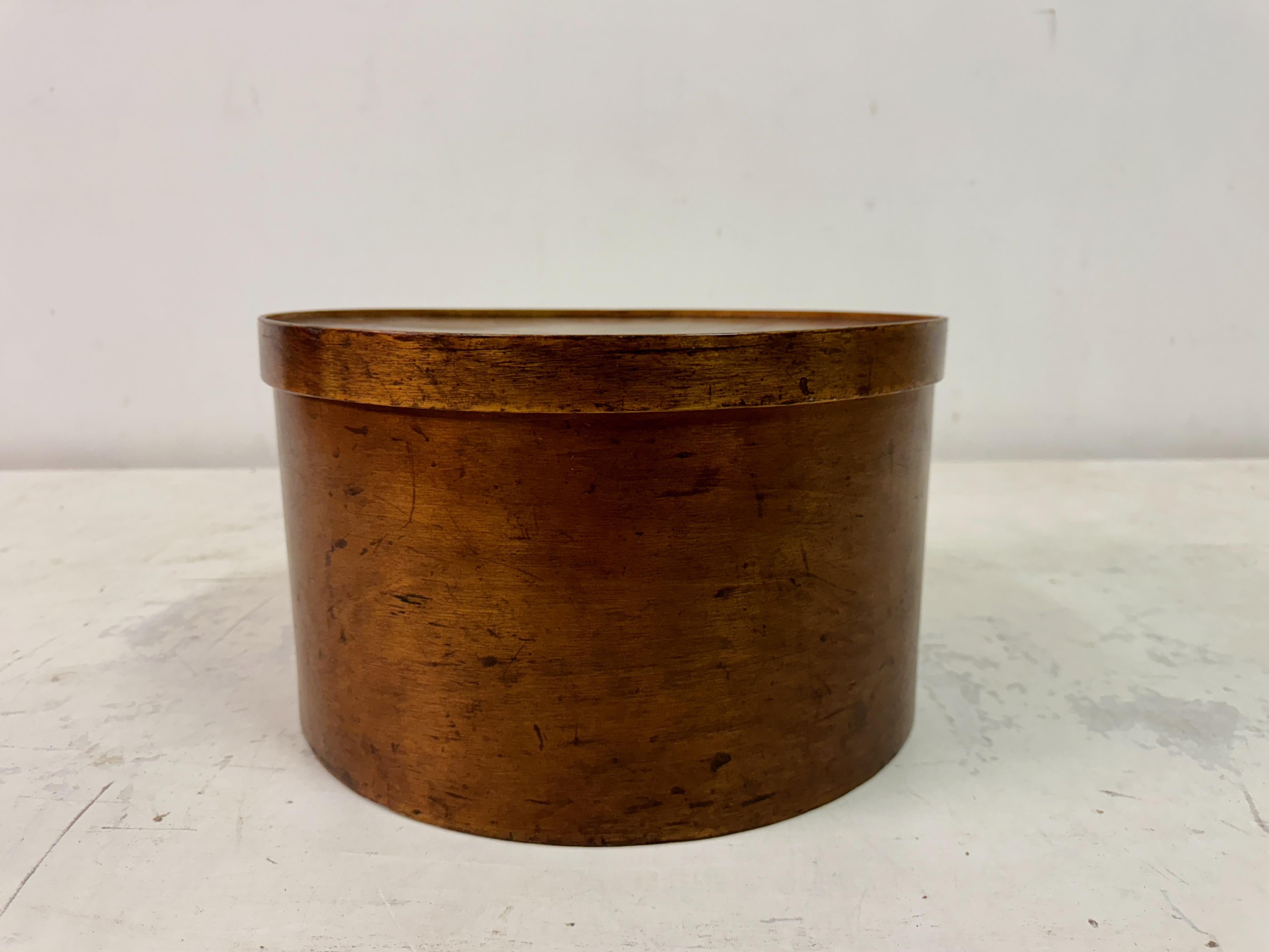 Caja vintage de madera curvada para sombreros

Se trata de una sombrerera vintage minimalista de madera contrachapada curvada, caracterizada por su forma cilíndrica lisa y su superficie sin adornos. El cálido tono marrón de la madera resalta su