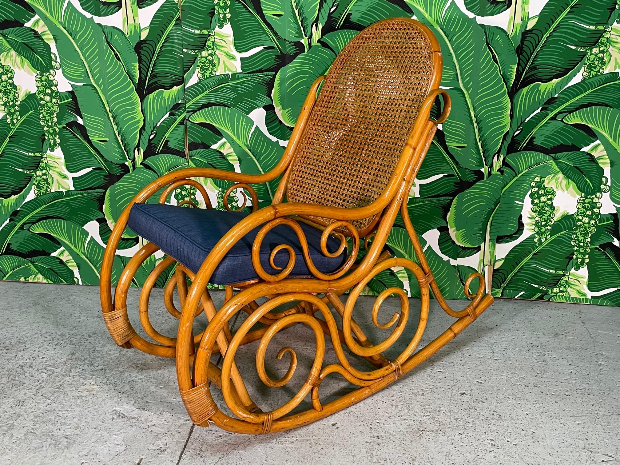 Vintage rattan rocker features ornate scrollwork, bentwood arms, and cane back and seat. Harkens the iconic Thonet chair. Good condition with minor imperfections: Cane seat has indentation and one small strapping at lower rear is missing.

     
