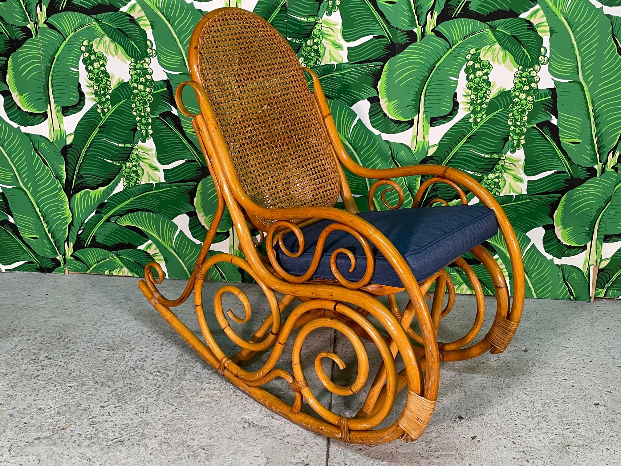 Vintage rattan rocker features ornate scrollwork, bentwood arms, and cane back and seat. Harkens the iconic Thonet chair. Good condition with minor imperfections: Cane seat has indentation and one small strapping at lower rear is missing.
 
 