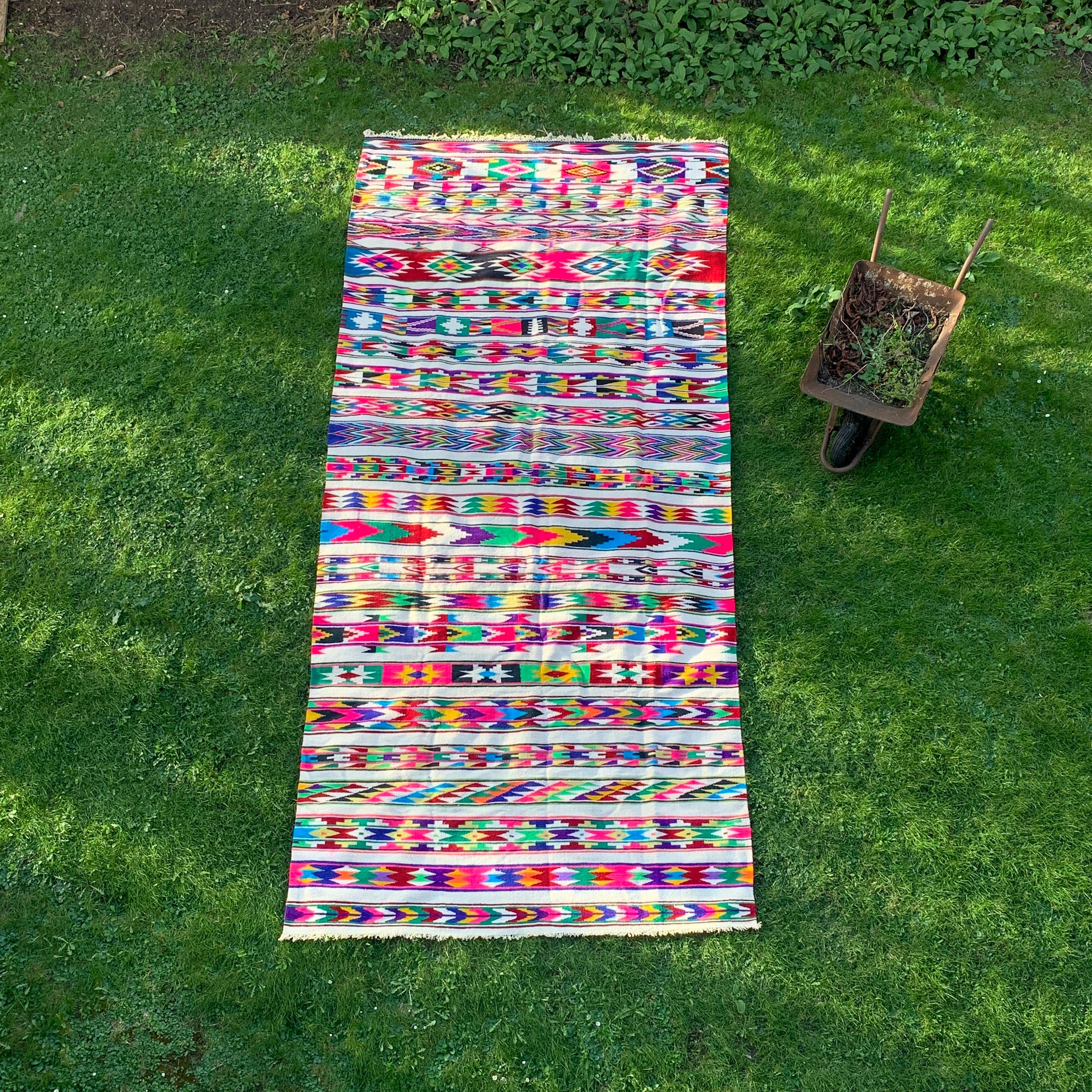 A very large Algerian Berber rug with many different colorful patterns, such as arrows, diamonds, triangles, and more, stacked and organized in horizontal lines on a white/beige base, is a stunning work of art that is characterised by its standout