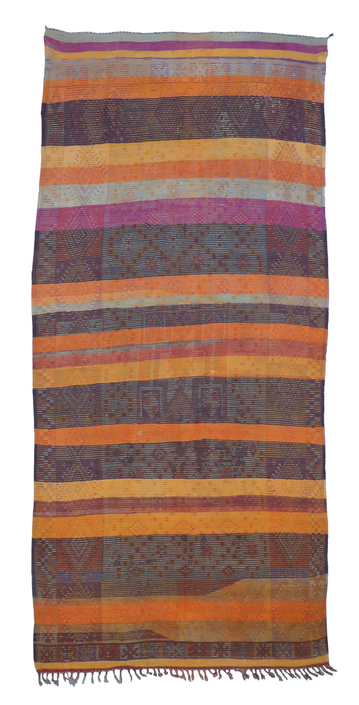 This is an exceptional vintage Znaga tribal flat-weave rug emblazoned with a field of earth tones and hand knotted motifs in brown, rust, orange, purple, olive, and red. There are a number of small repairs that match the original premium quality of