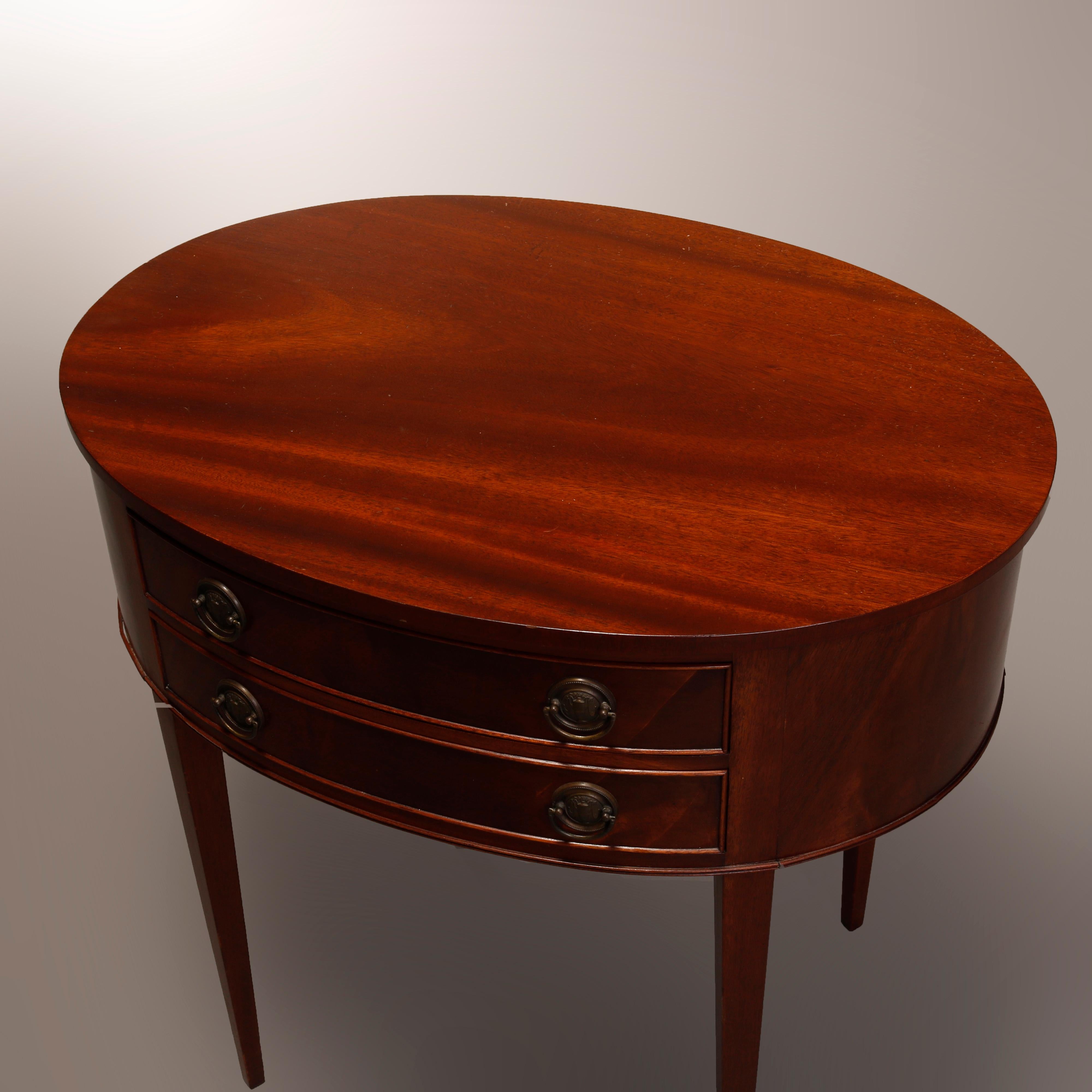 A vintage side table in the manner of Berkey & Gay offers oval form in Hepplewhite style with flame mahogany construction having double drawer case raised on tapered and straight legs, circa 1940

Measures: 27