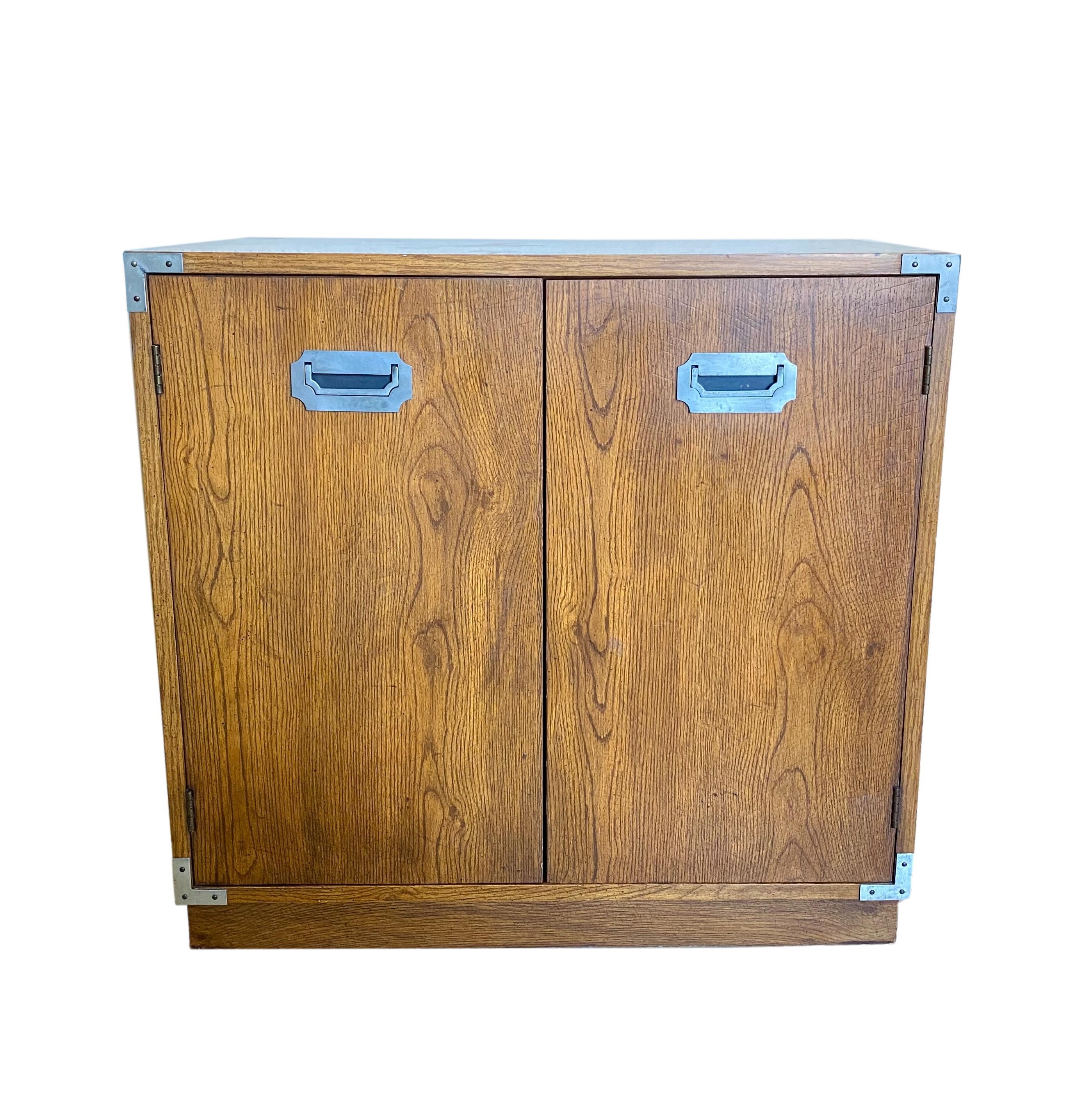 A vintage 1970's campaign style 2-door storage cabinet by Bernhardt. Wood and wood veneer with nickel plated hardware; one removable interior shelf.

Dimensions: 30