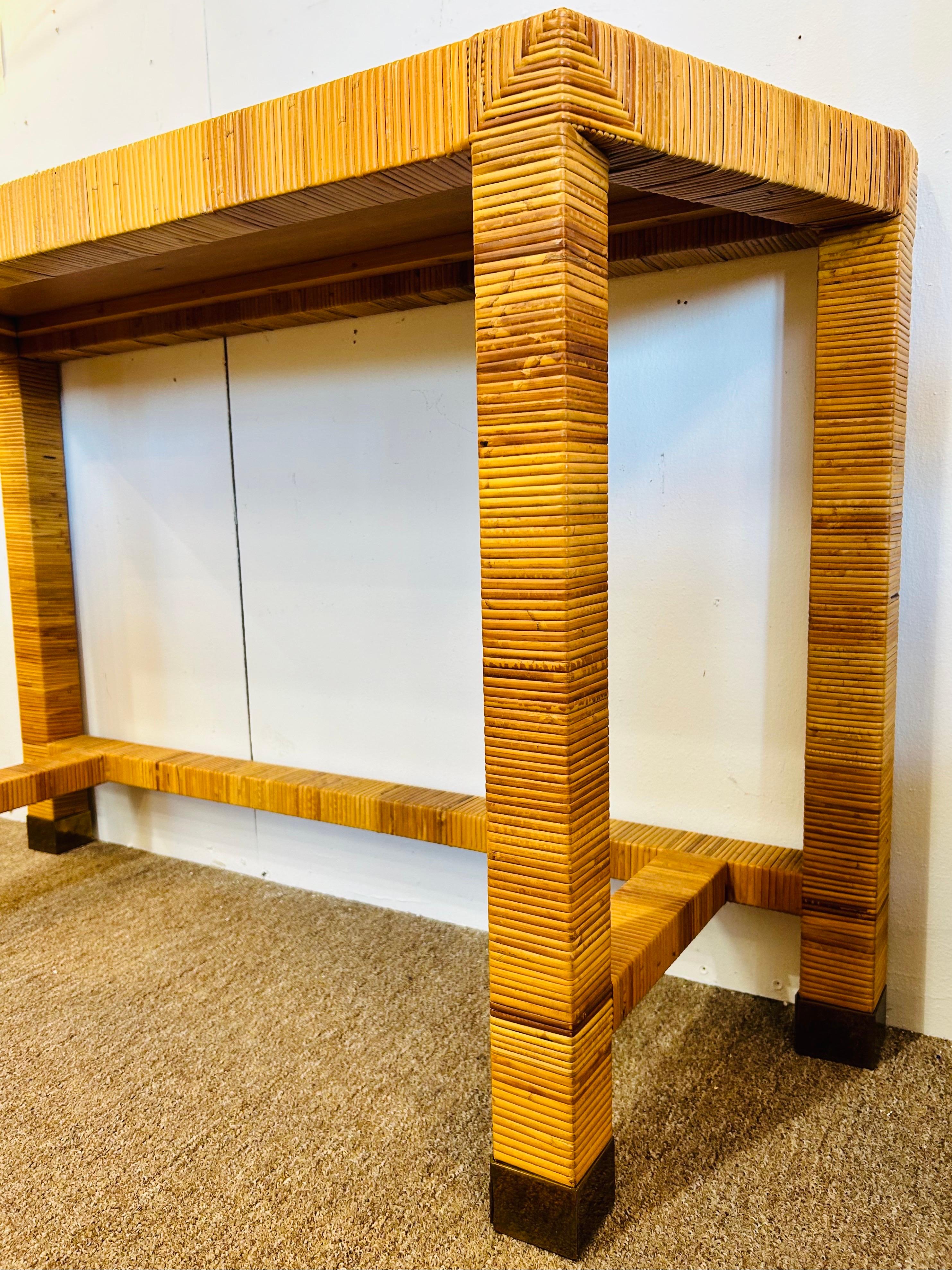 A vintage 1980's Bielecky Brothers style rattan wrapped and woven cane trapezoid shaped console table. The square shaped legs add a sturdy linear design to the angle shaped top. The brass capped feet ground the piece in timeless style adding a bit