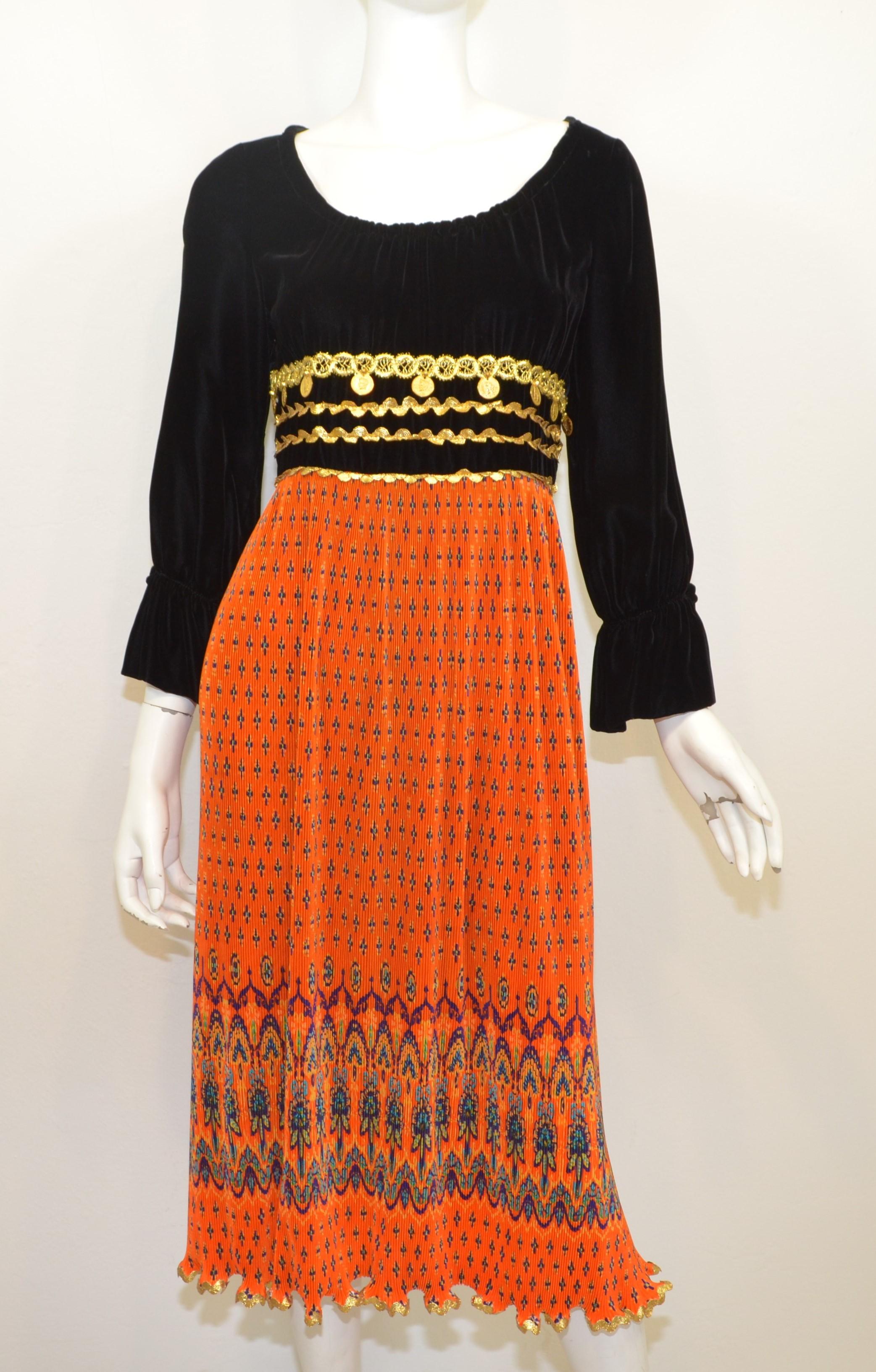 Vintage Bill Blass dress features a black velvet top half with a tie detail on the sleeves, metallic gold threading and dangling coin embellishments. Skirt is featured in a vibrant orange with a pleated design and mixed pattern throughout. Dress has