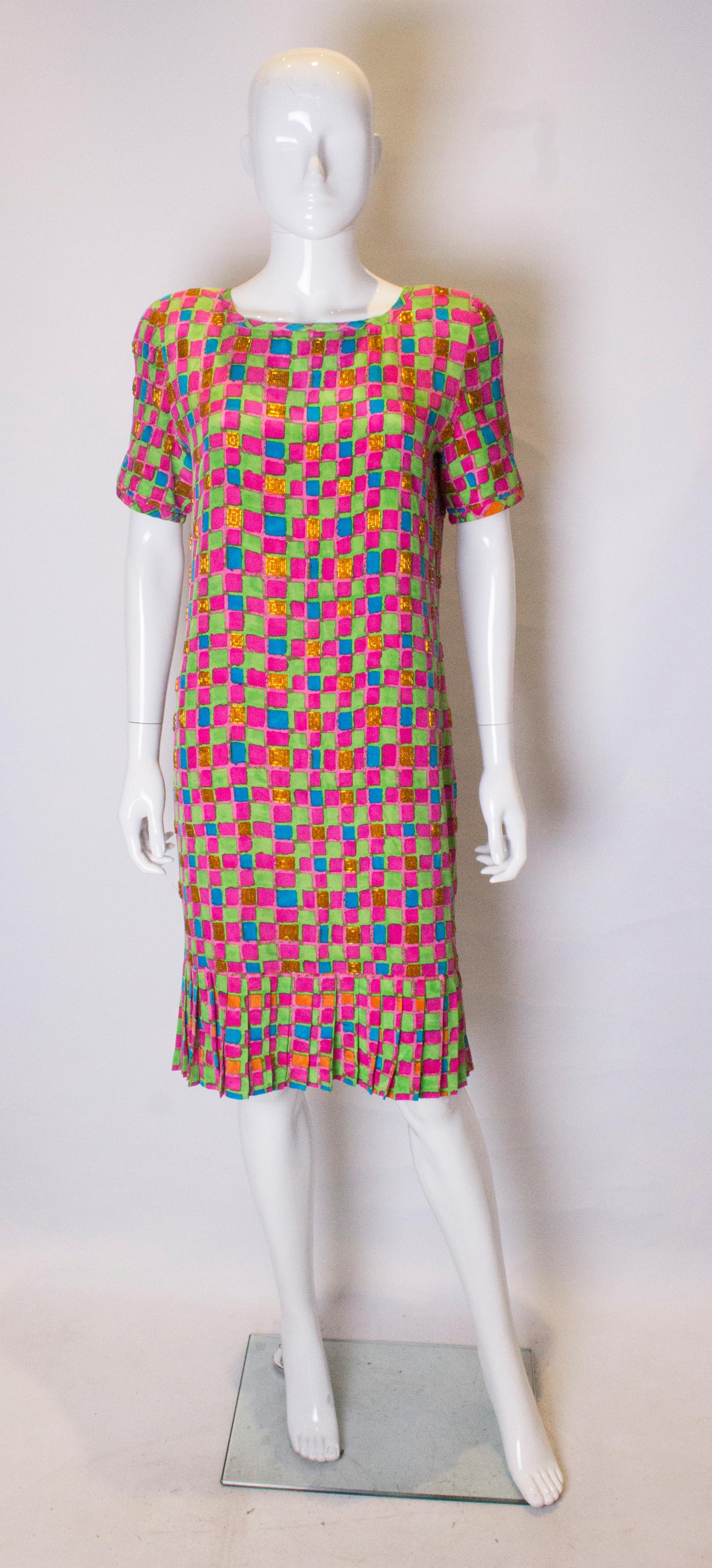 A chic and colourful dress by Bill Blass. The dress is in a colourful print of pink,blue,green and orange with bead decortaion. It has a drop waist and pleats at the hem. It is fully lined with a central back zip.
