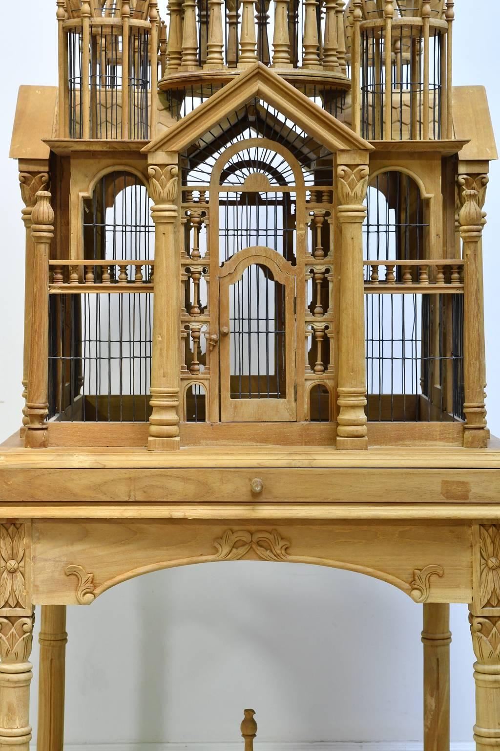 A very lovely and functional bird cage in raw teak wood. The elaborate design includes a main center cupola supported by carved columns that is surrounded by four smaller cupolas, all topped with turned steeples. Each of the four sides offers access