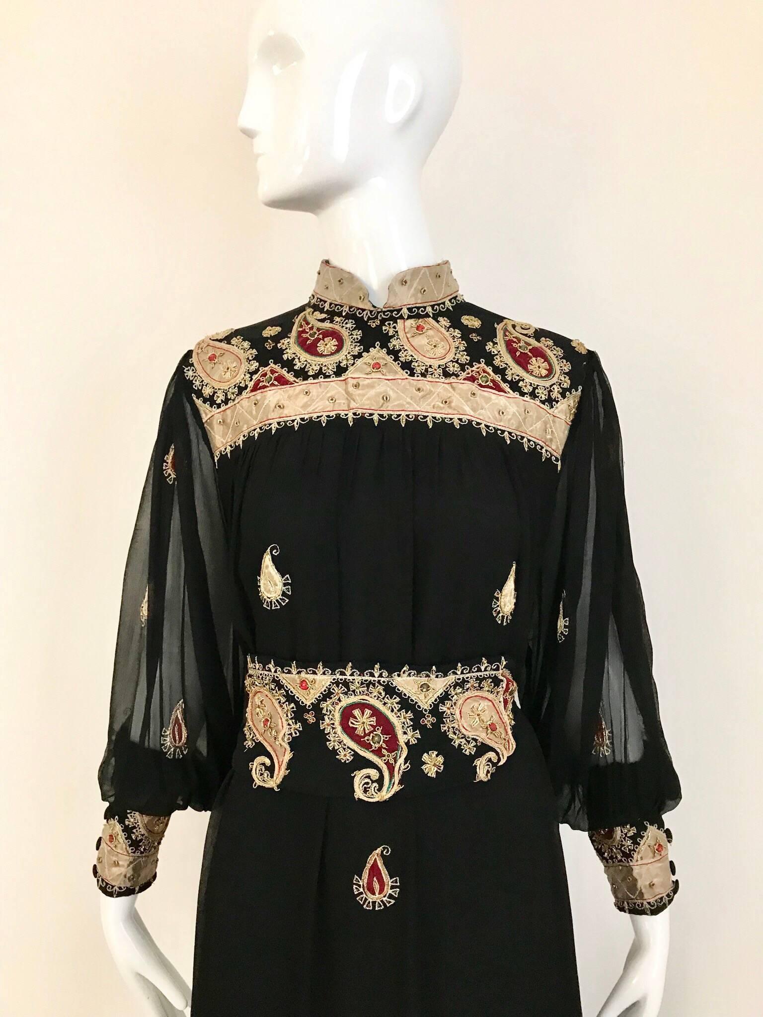 This 1970s Neiman Marcus black silk kaftan maxi dress has an ethnic feel from the gold paisley embroidery in the applique and the nehru collar, giving it a distinct Indian flavor. The billowy sleeves sport wide cuffs with more embroidery. And the