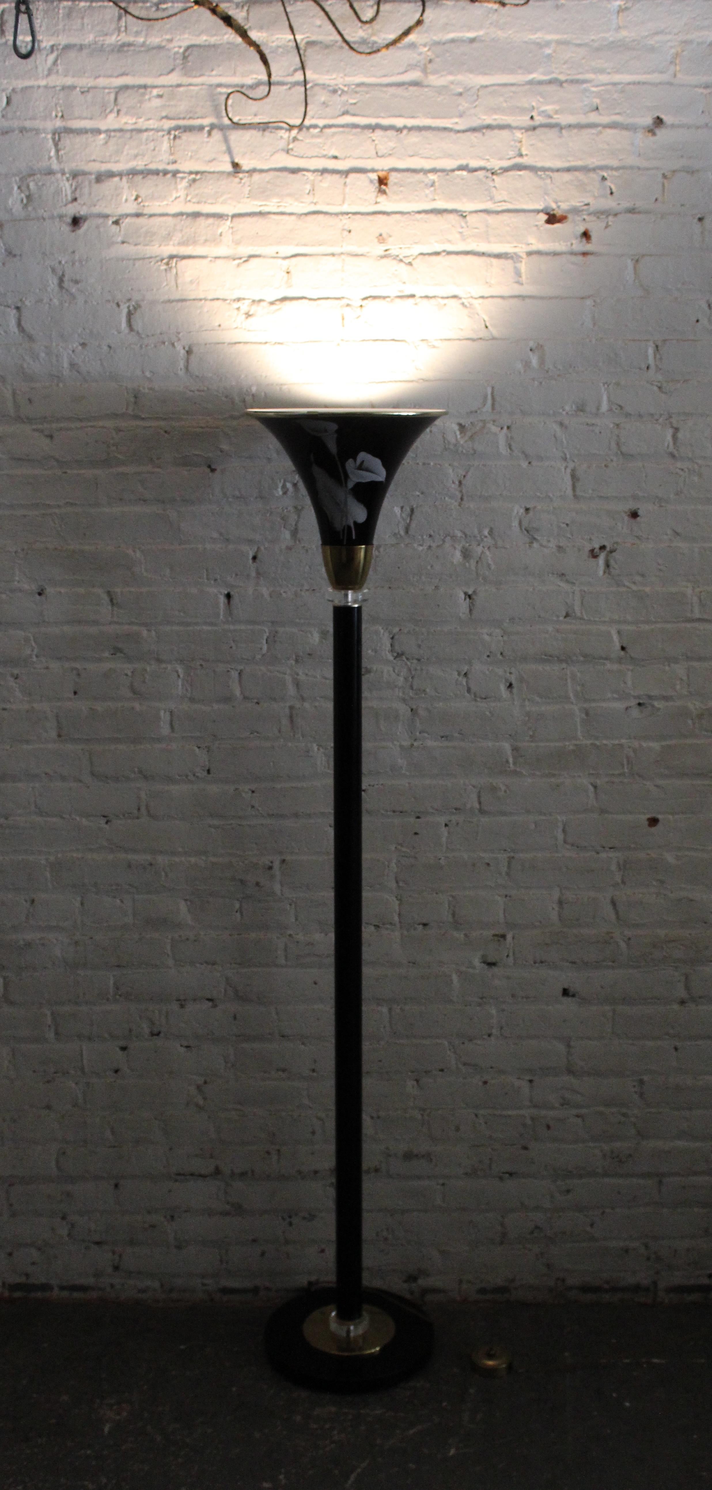Llamativa lámpara de pie antorcha vintage con un acabado lacado en negro de alto brillo con detalles de latón pulido y una pantalla acampanada adornada con calas blancas pintadas a mano. Un detalle de lucita transparente en el cuello y un