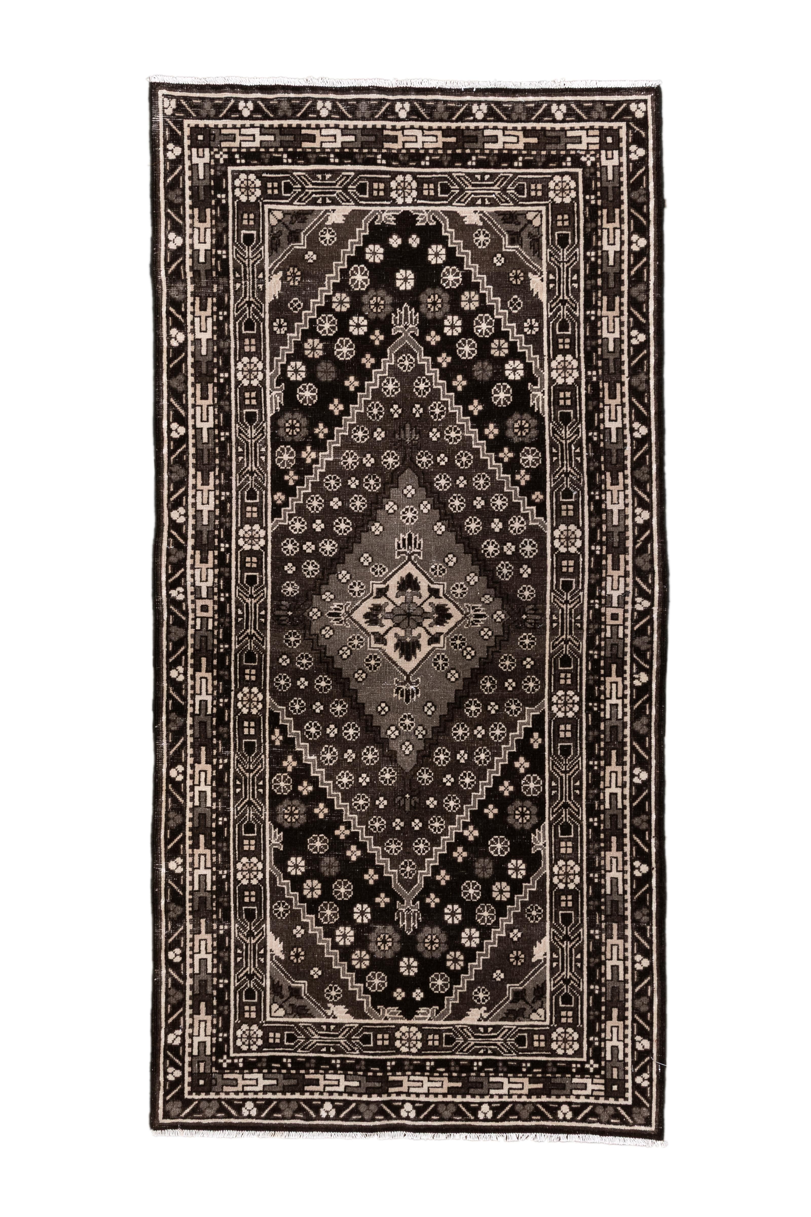 A striking vintage Khotan rug from East Turkestan, featuring a bold palette of black, ivory, and soft taupe. The field is centered with a stepped diamond medallion surrounded by geometric flower motifs and guarded by a classic Khotan border with