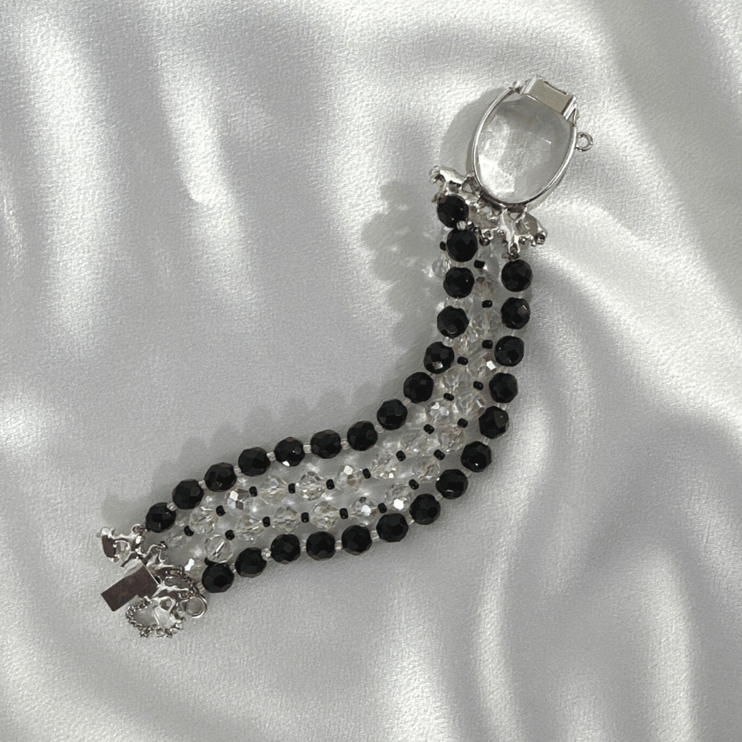 A Striking Contrast of Elegance and Design
This vintage statement bracelet is a masterclass in contrast and composition, blending black and white lucite beads with a stunning oval-cut clear crystal centerpiece. The bracelet’s structure is defined by