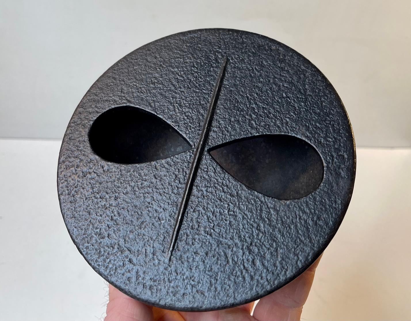 A mysterious cast iron lidded bowl, incenser or ashtray. It has a textured black treatment and features a lid shaped as a mask. A curious modernist or brutalist piece made in Sweden circa 1960-65. Measurements: Diameter: 15 cm, Height: 5.5 cm.