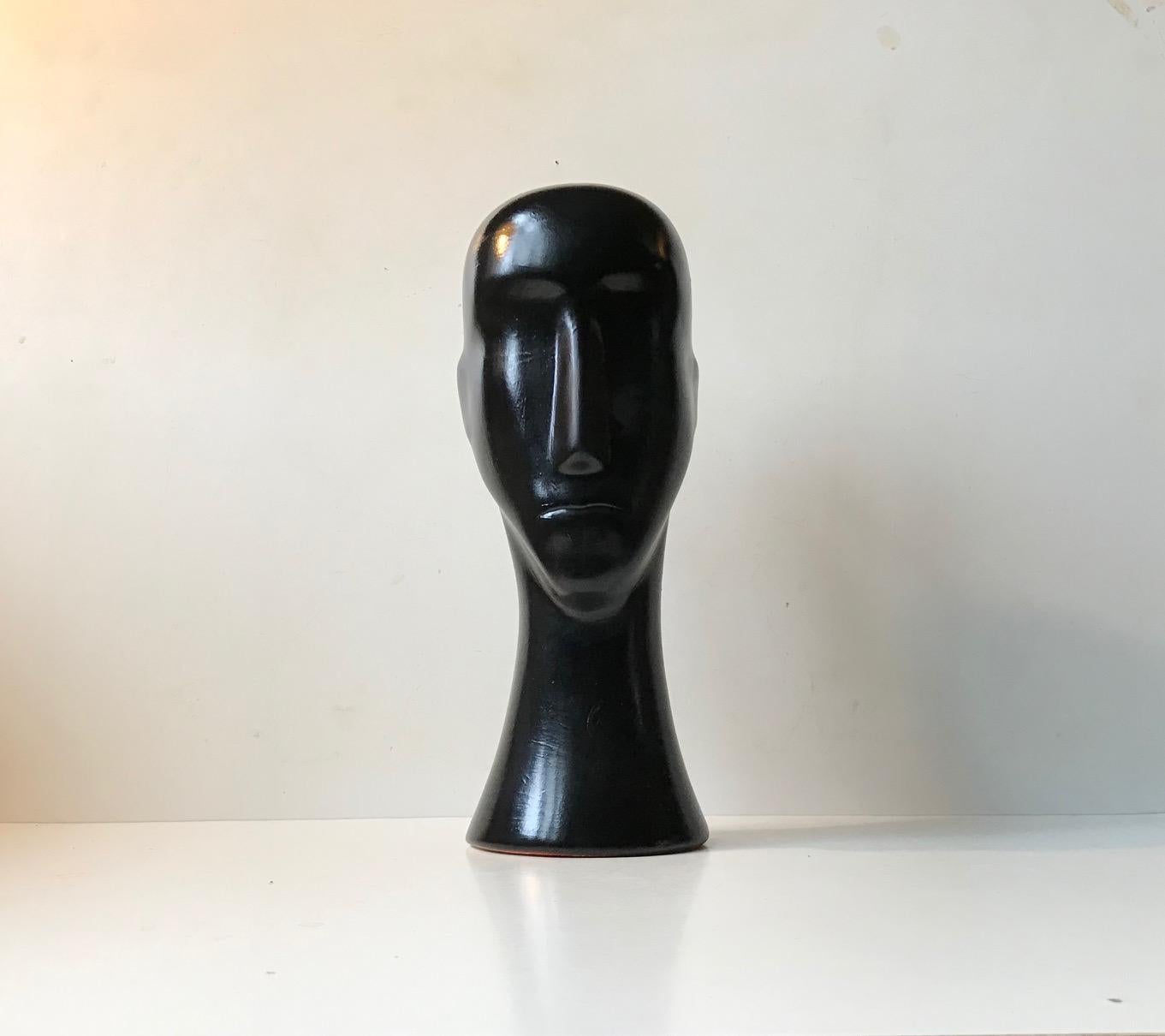This abstract head has an expressionless face with a long flat nose, simple indents for eyes, a small slit mouth and bald head. It's sculpted to let light and shadow create its features depending on the angle of viewing. The overall appearance of