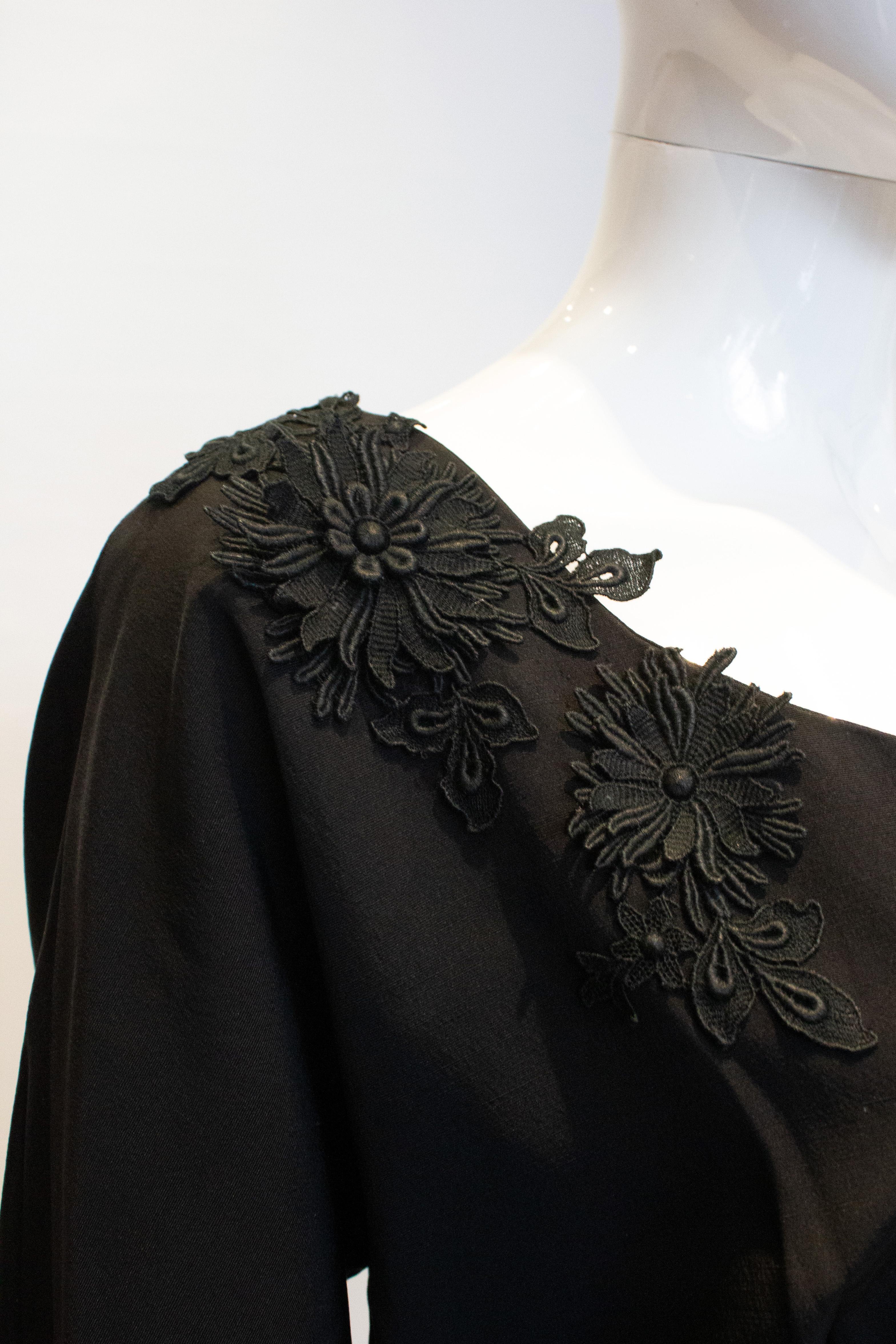 Une robe de cocktail noire chic et vintage, créée par H Tromp pour Melonique Originals Ltd.
La robe est en tissu côtelé avec un dos en V, une ceinture en tissu et des appliques florales. Il a une ouverture zippée sur le côté, et n'est pas doublé.

