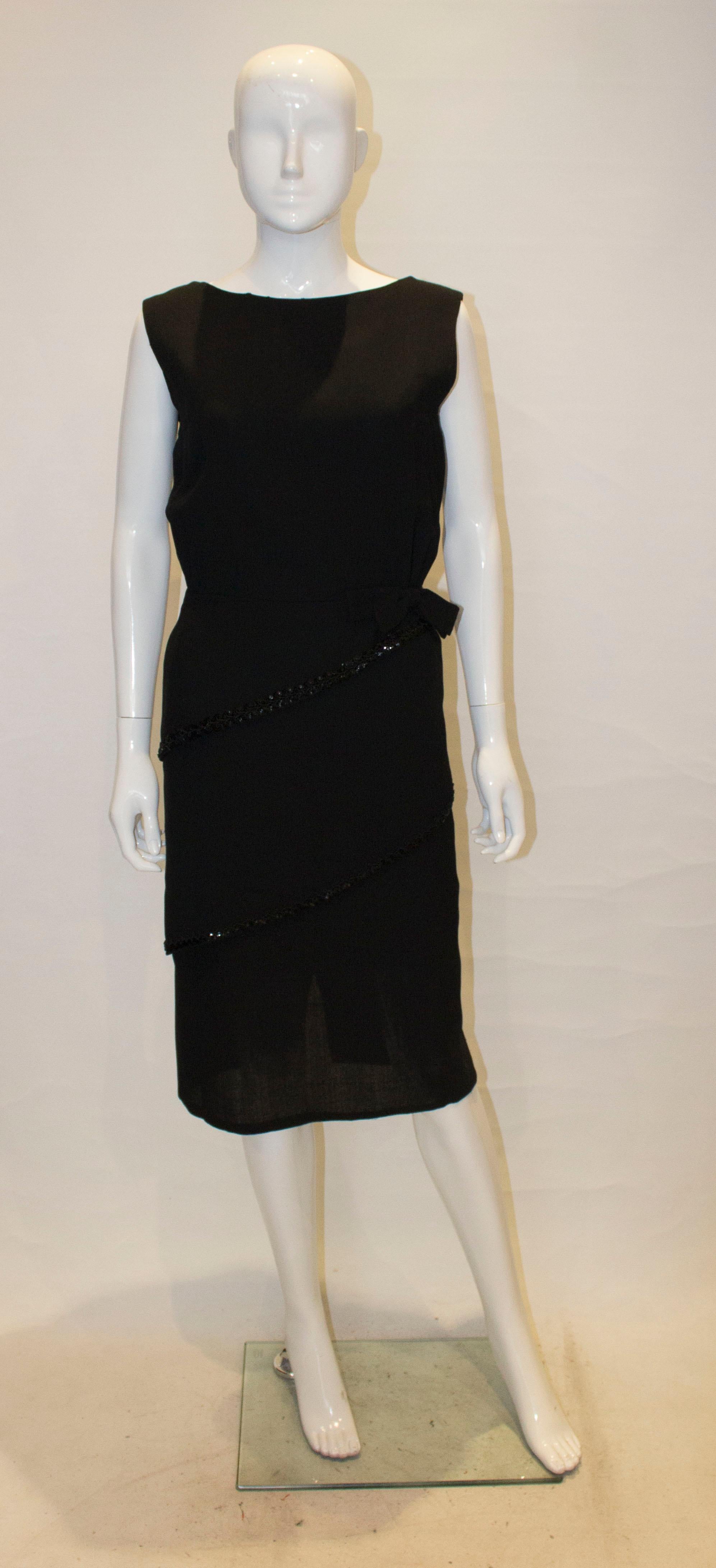 A black crepe dress with sequin trim by Schroder Wulf. This dress is sleavless with a round neckline, a bow at waist leval and asymetric layers . It is  fully lined.