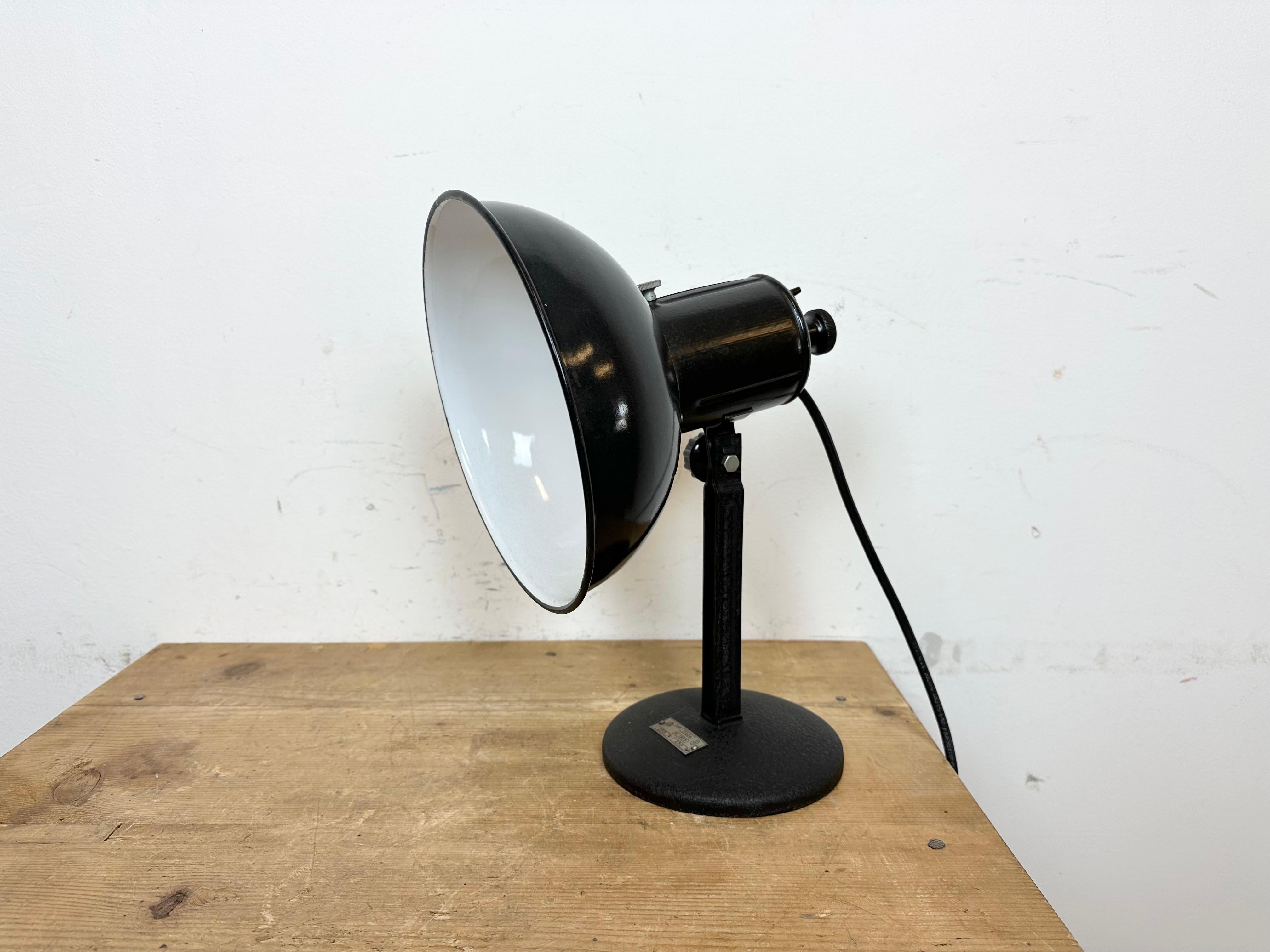 Vintage Industrial adjustable table lamp from former Czechoslovakia made during the 1950s. Was used in photo studios. It features a black enamel shade with white enamel interior an iron arm and base.The original porcelain socket requires standard E