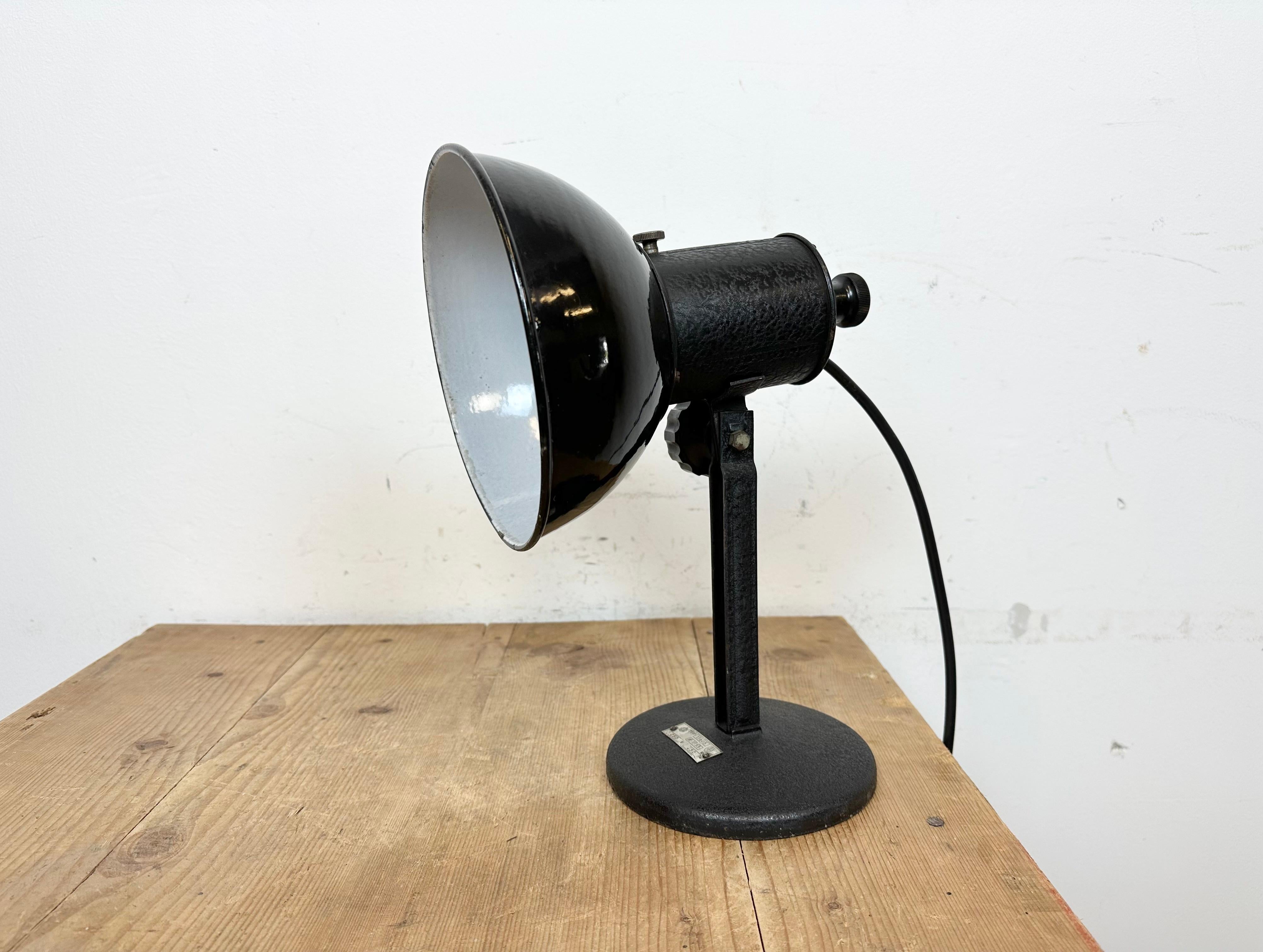 Vintage Industrial adjustable table lamp from former Czechoslovakia made during the 1950s. Was used in photo studios. It features a black enamel shade with white enamel interior an iron arm and base.The original porcelain socket requires standard E