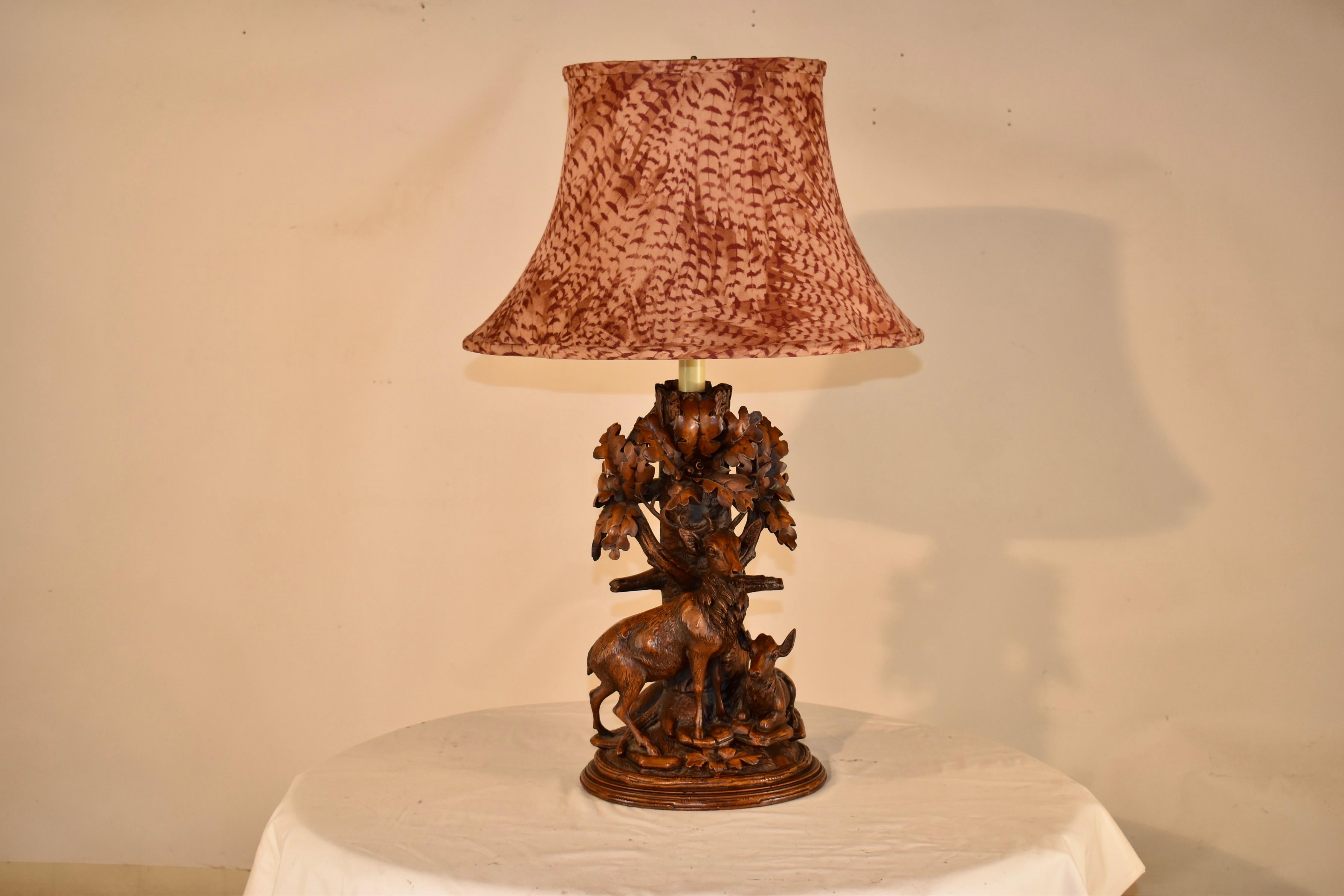 Meravigliosa lampada in fusione nello stile Black Forest di intaglio del legno.  La lampada raffigura un albero sullo sfondo con un cervo in piedi e una cerva sdraiata accanto a lui.  Si trovano su un letto che sembra il suolo della foresta, pieno