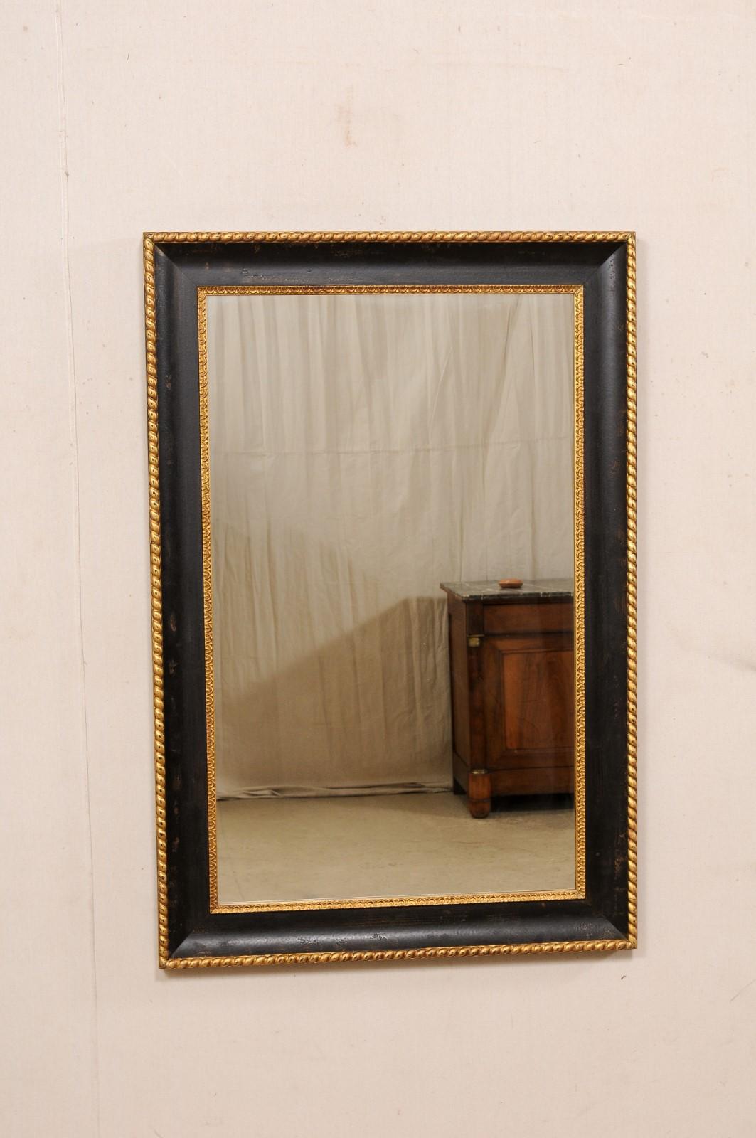 A vintage American carved and painted wood mirror. This rectangular-shaped mirror has a black wood frame, which has been embellished with gold gilt lamb's tongue trimming about the inner surround (next to the glass), and a gold rope twist carved