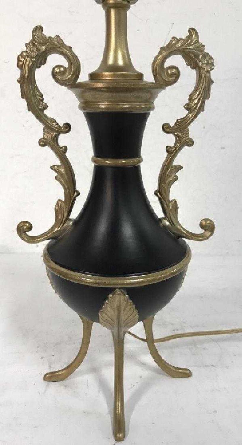 The vintage classical urn-shaped lamp has a black body and gold toned legs, rings and a pair of ornate detailed handles with 