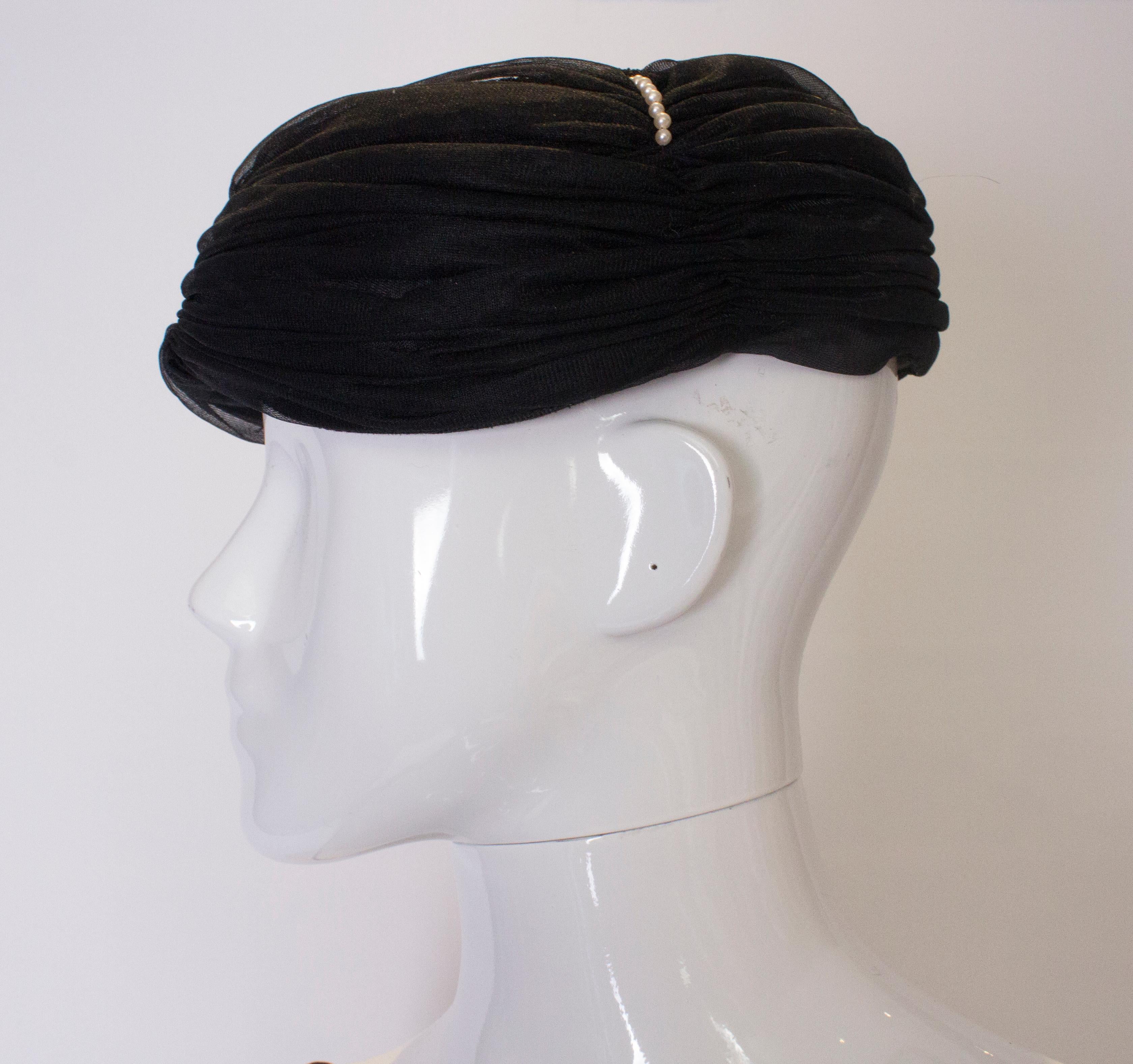 A chic black hat with gathered fabric and  four rows of pearl detail on the crown. Inner circumference 22''.