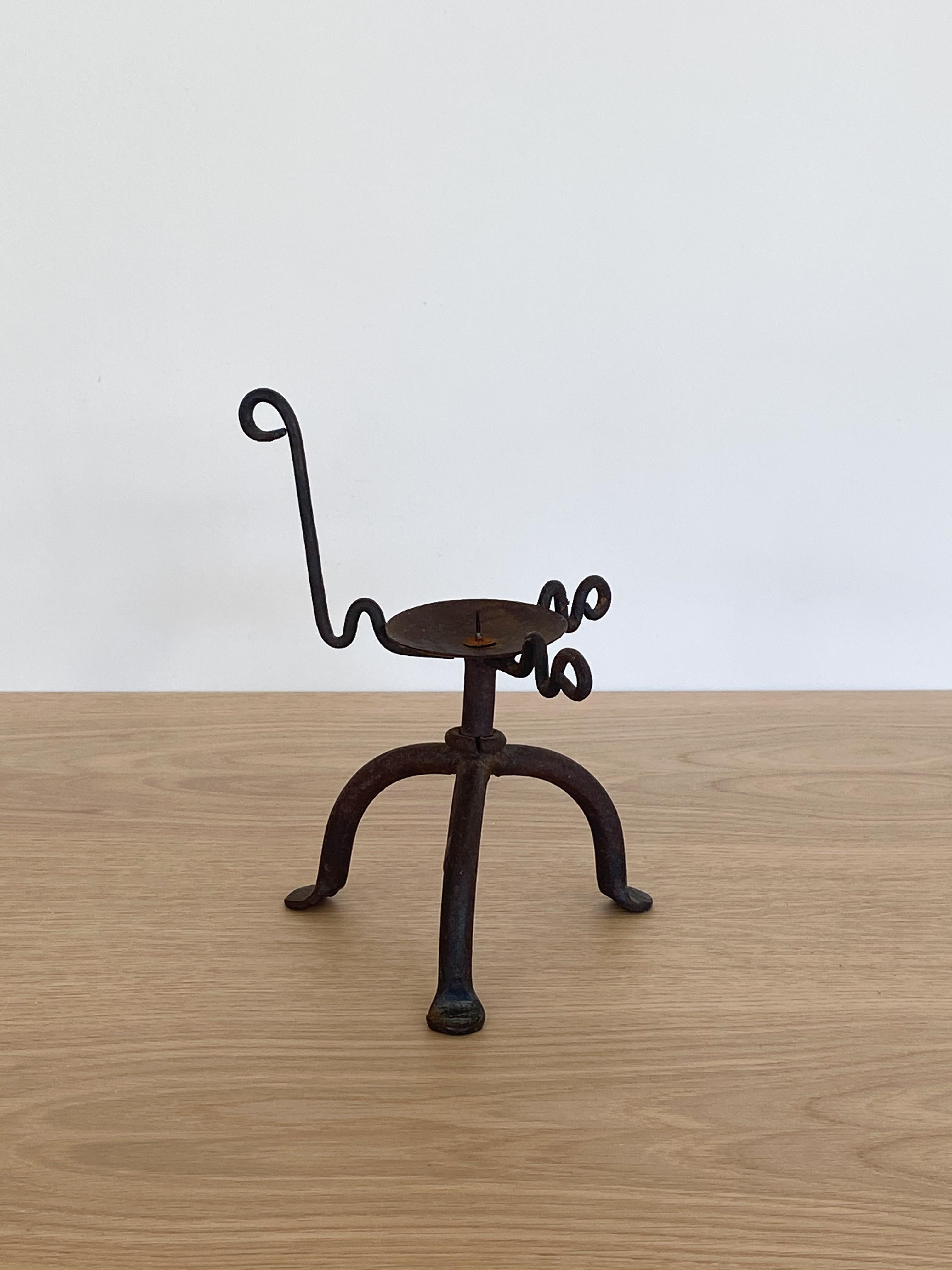 Vintage black iron candlestick holder with 3 squiggly arms and tripod legs. Original finish shows patina and rust.