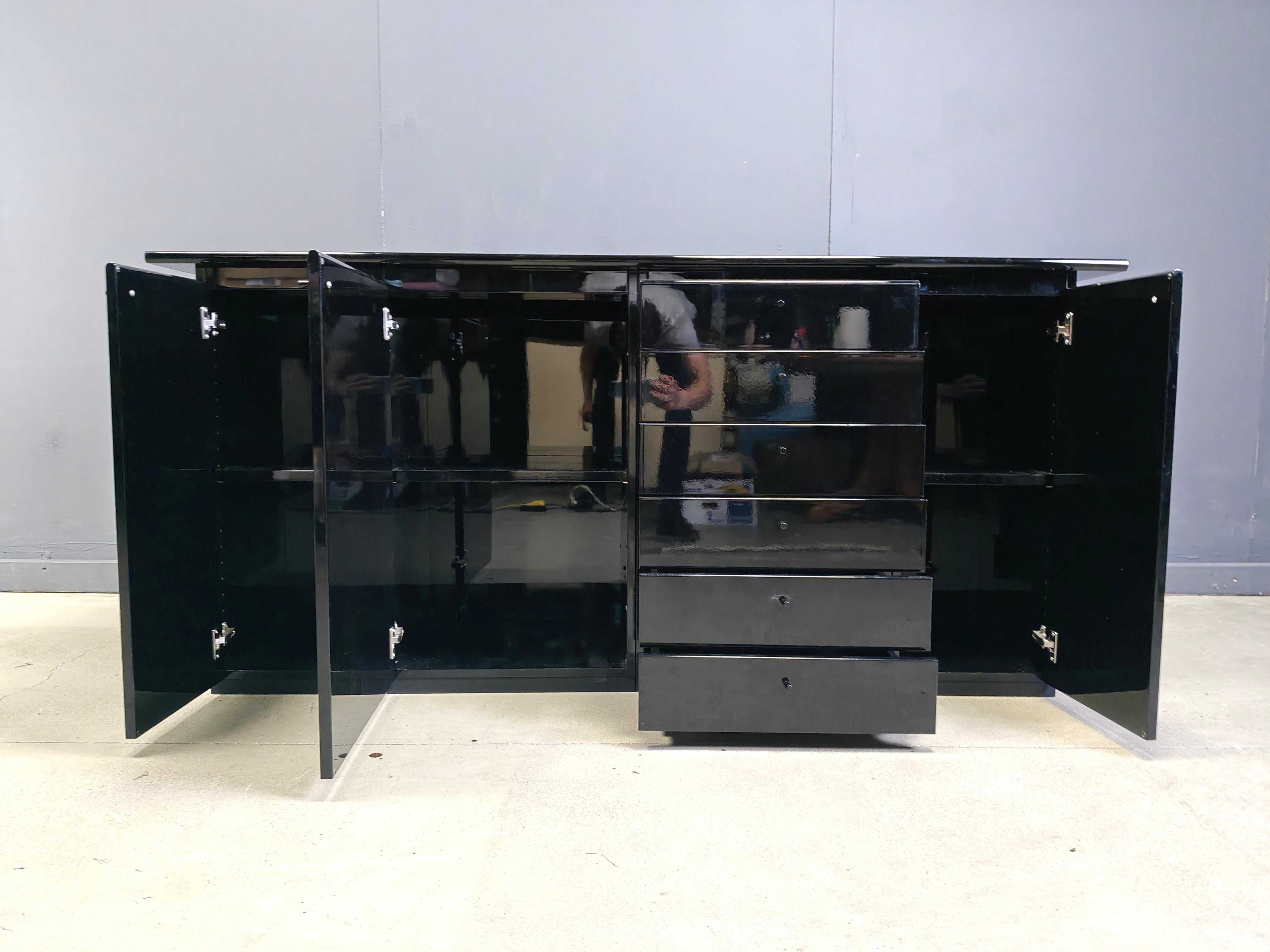 Shiny black lacquered seventies sideboard with three doors and 6 drawers.

Whilst being compact in size, it still offers plenty of storage space.

Original seventies cabinet, but still very up to date and very well manufactured.

Good condition with