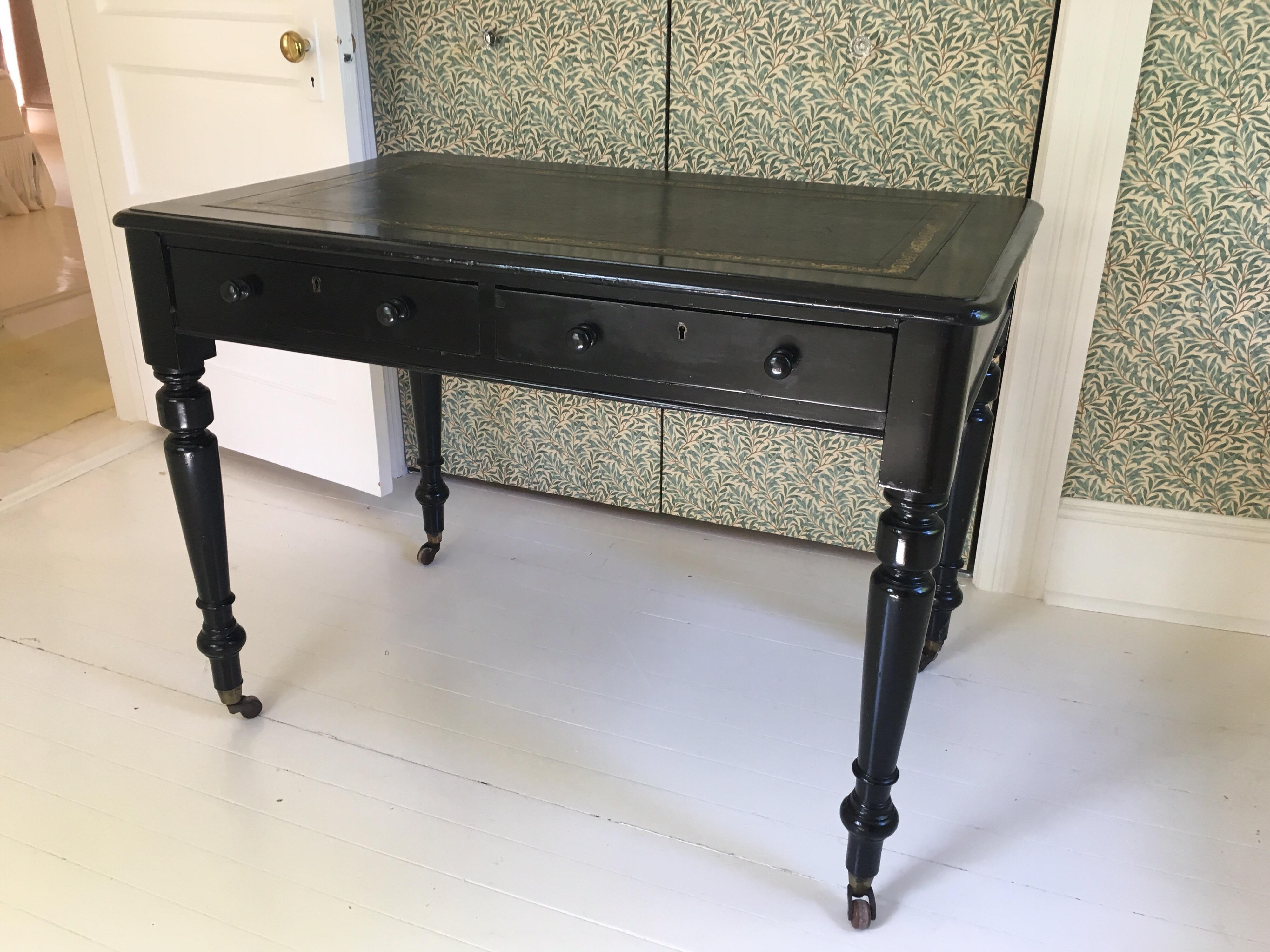 Vintage black lacquered desk with leather top on turned wooden legs and brass casters. Two center drawers on one side.
General wear to top and finish.
Measures: 40.75