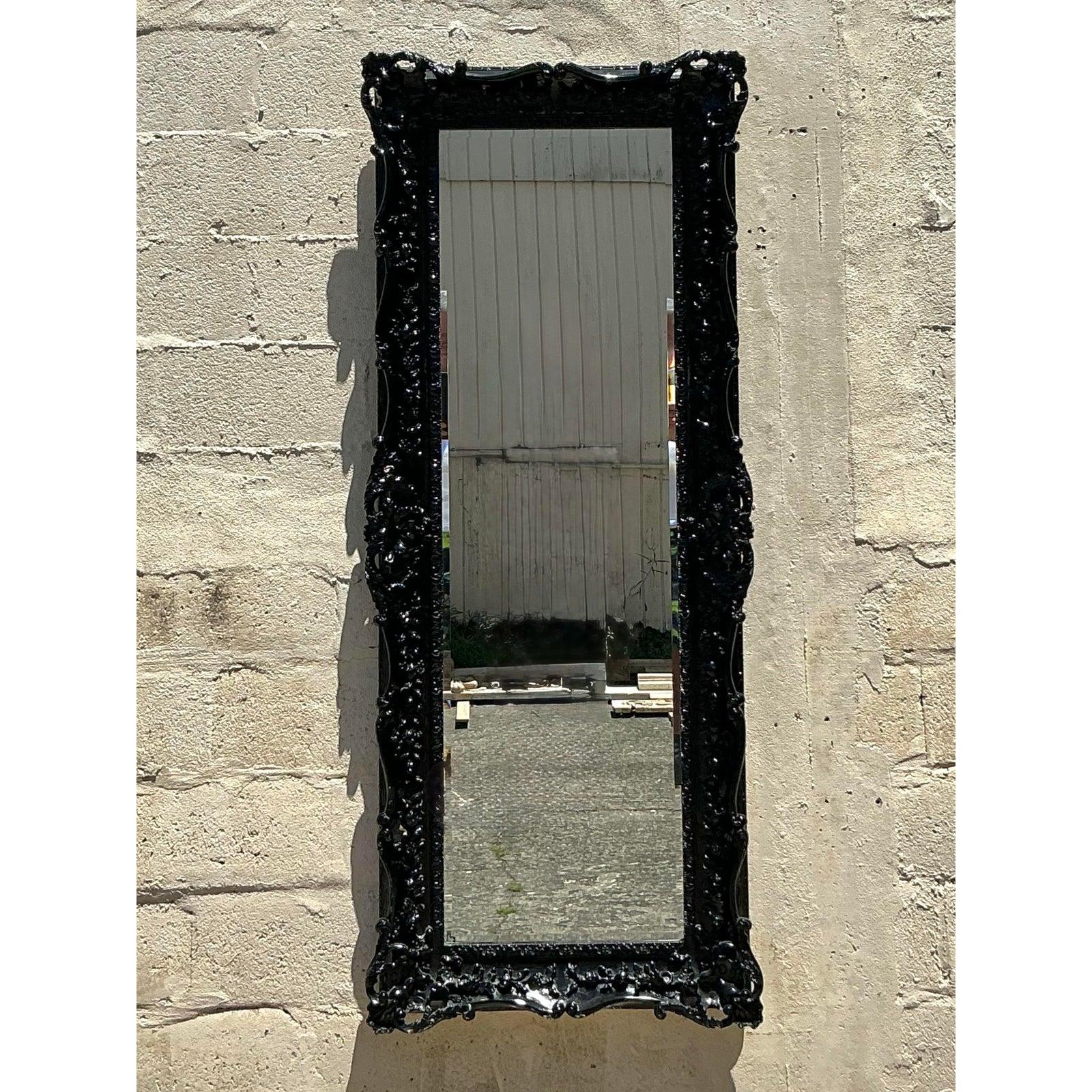 Atrévete con este llamativo espejo rococó vintage, con un marco ornamentado de estilo barroco acabado en laca negra de alto brillo. Las intrincadas tallas florales y la espectacular silueta evocan la opulencia europea del siglo XVIII, mientras que