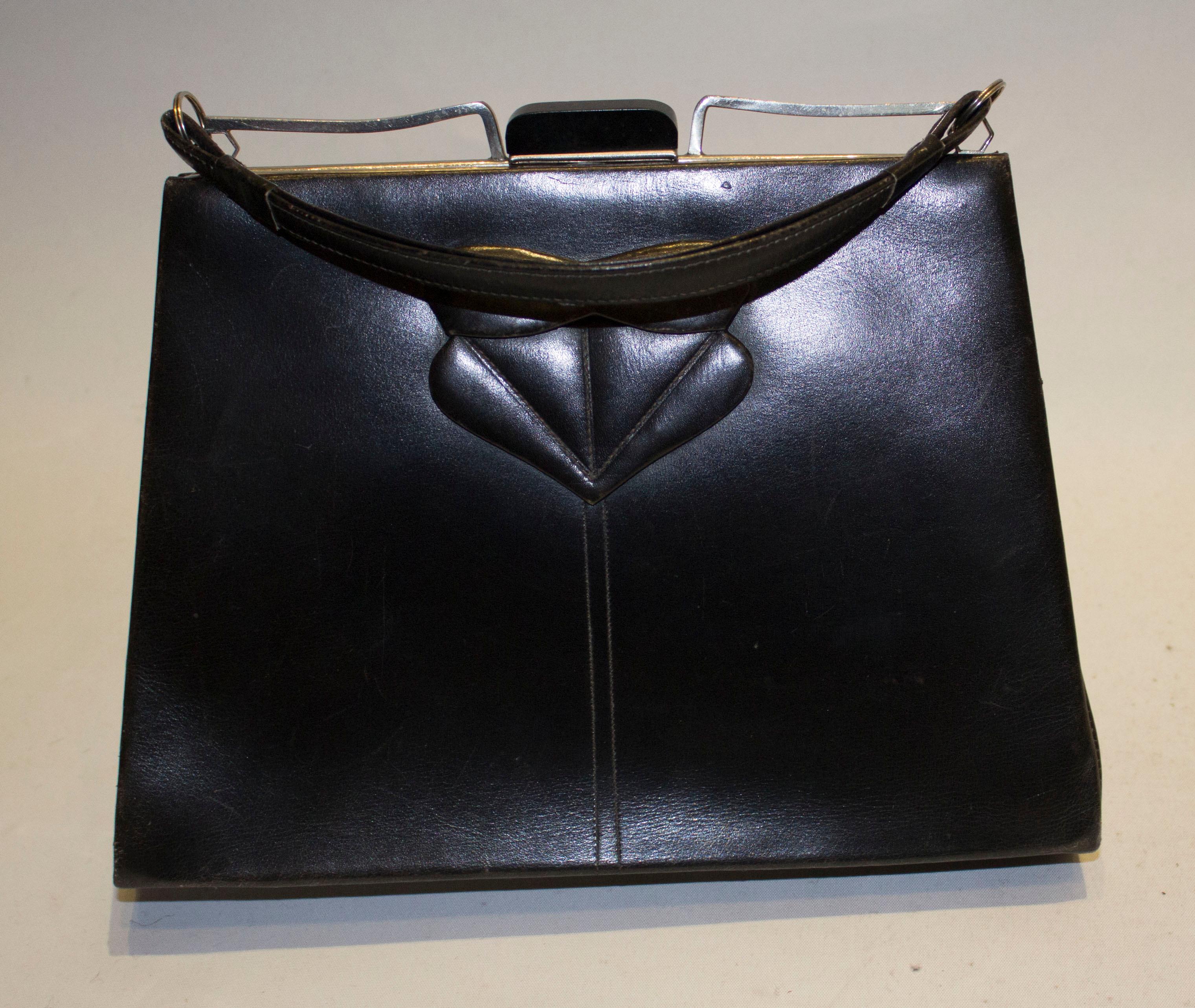 A chic vintage black leather art deco bag. The bag has attractive detail on the front ,and the top clasp. Inside there are two compartments , one with a pouch pocket and one with a purse pocket. The bag has a leather handle and measures width 9 1/2