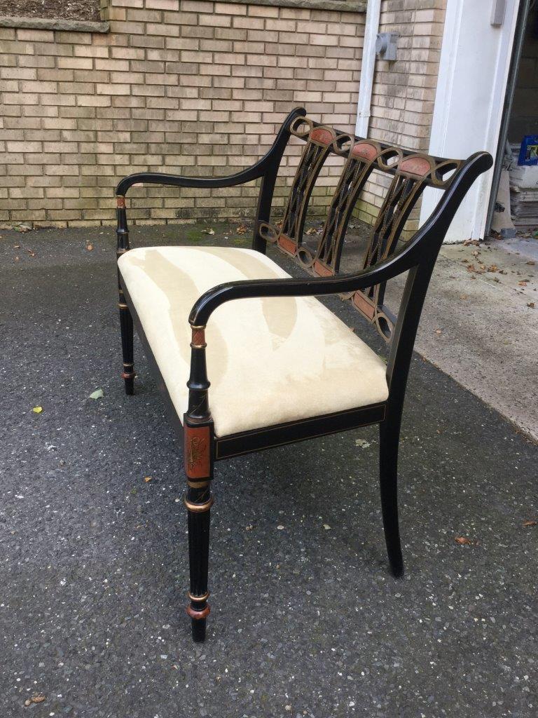 A glamorous painted bench having a black laquered frame and an open scroll back with a trellis motif. There are many painted decorative touches in gold and red throughout the frame, including the back, arms, and legs. Newly upholstered in a cream