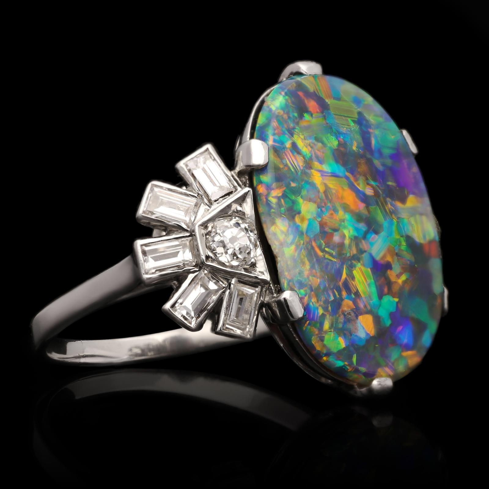 A beautiful black opal and diamond cocktail ring c.1950s, centred with an oval Australian black opal cabochon with a dark body colour and wonderful play of colour with all the spectral colours from red through to violet, claw set in platinum between