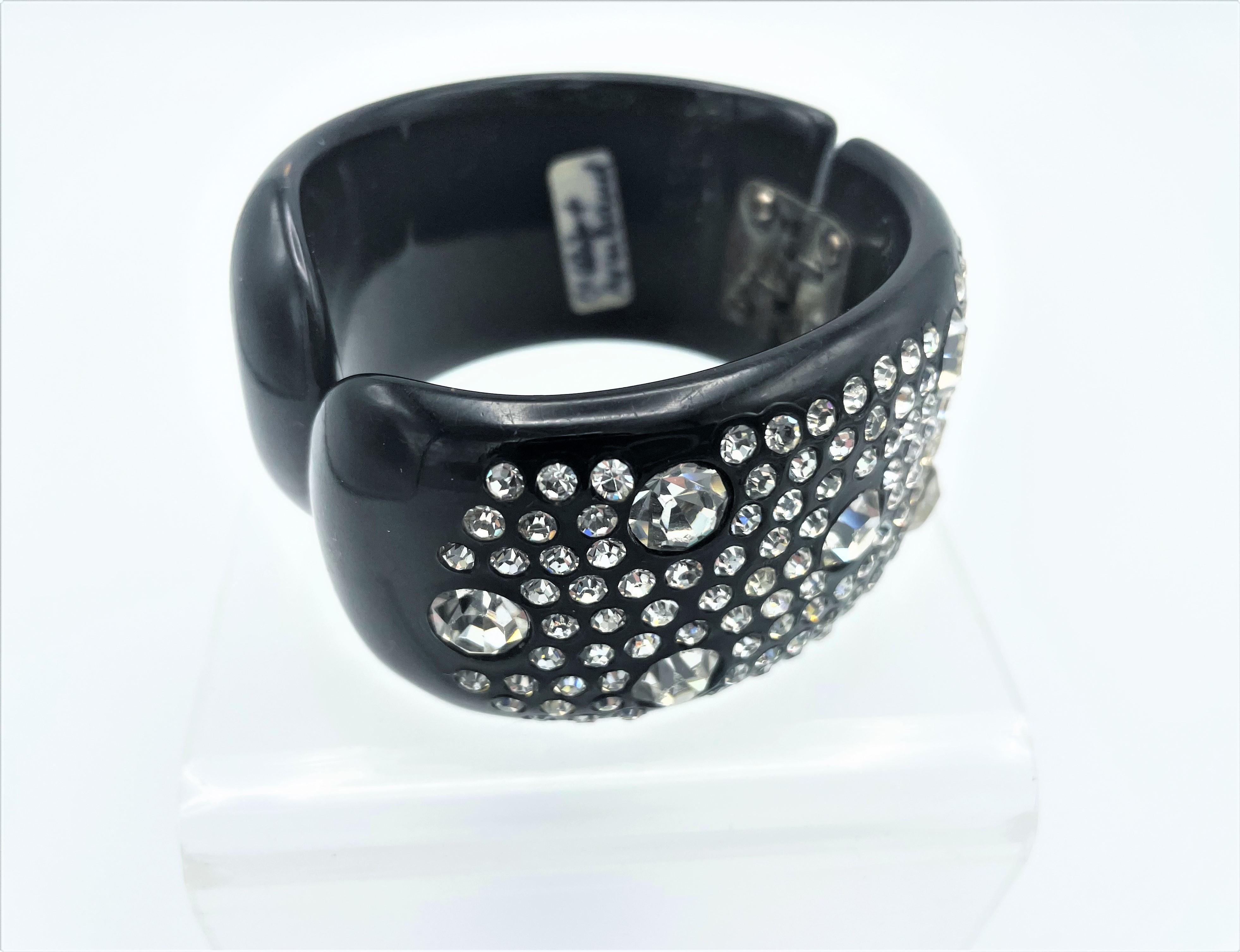 
Very decorative black plastic bangle, side opening. The front is fully occupied with small and 6 large cut rhinestones. Front and back connected by a hinge and opening, so it fits almost every wrist.

Measurement: Width of the bangle 3,5 cm.