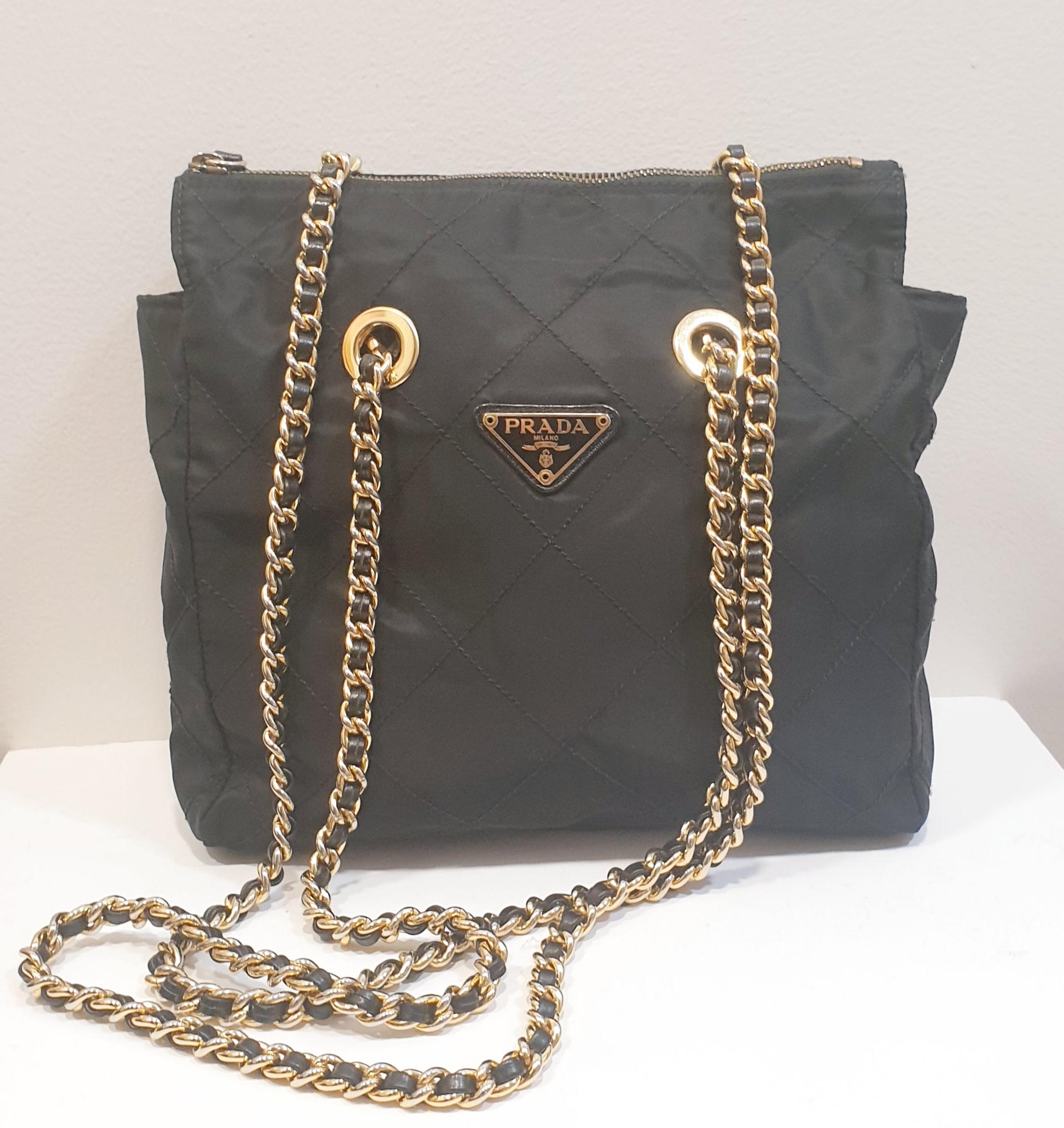 Prada original bag in black color with a double gold 
This tote has a quilted nylon body, woven leather chain straps, a top zip closure, and an interior zippered pocket. 
Italy 1980s-1990s
Color: Black
Material  Nylon
Lenght: 25 cm/ 9,84