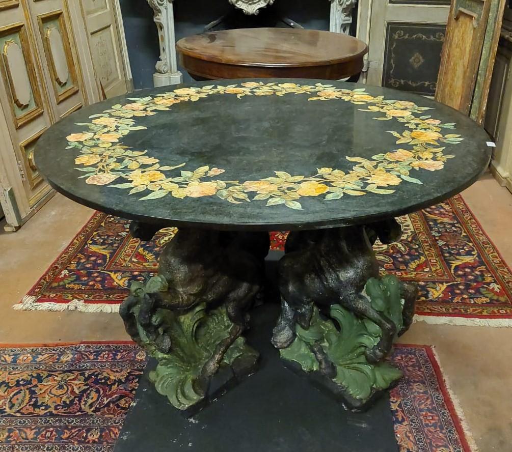 Vintage and antique round table, painted black background and prevalence, with sculpted and lacquered scagliola decorations. Inlaid plank, and base with four sculpted rampant horses, built in the first quarter of the 20th century in Italy,