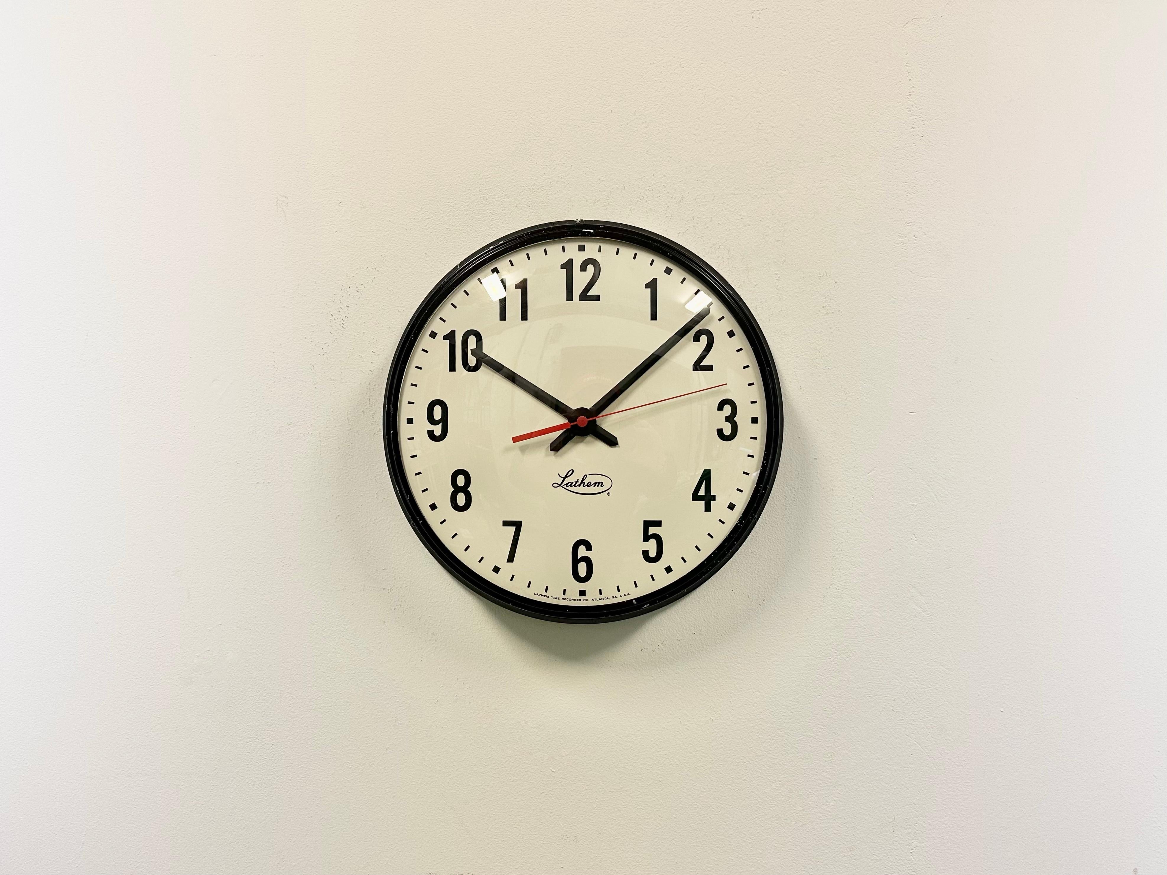 This wall clock was produced by Lathem in United states during the 1980s. It features a black metal frame, a metal dial and a convex clear glass cover. The piece has been converted into a battery-powered clockwork and requires only one AA-battery.