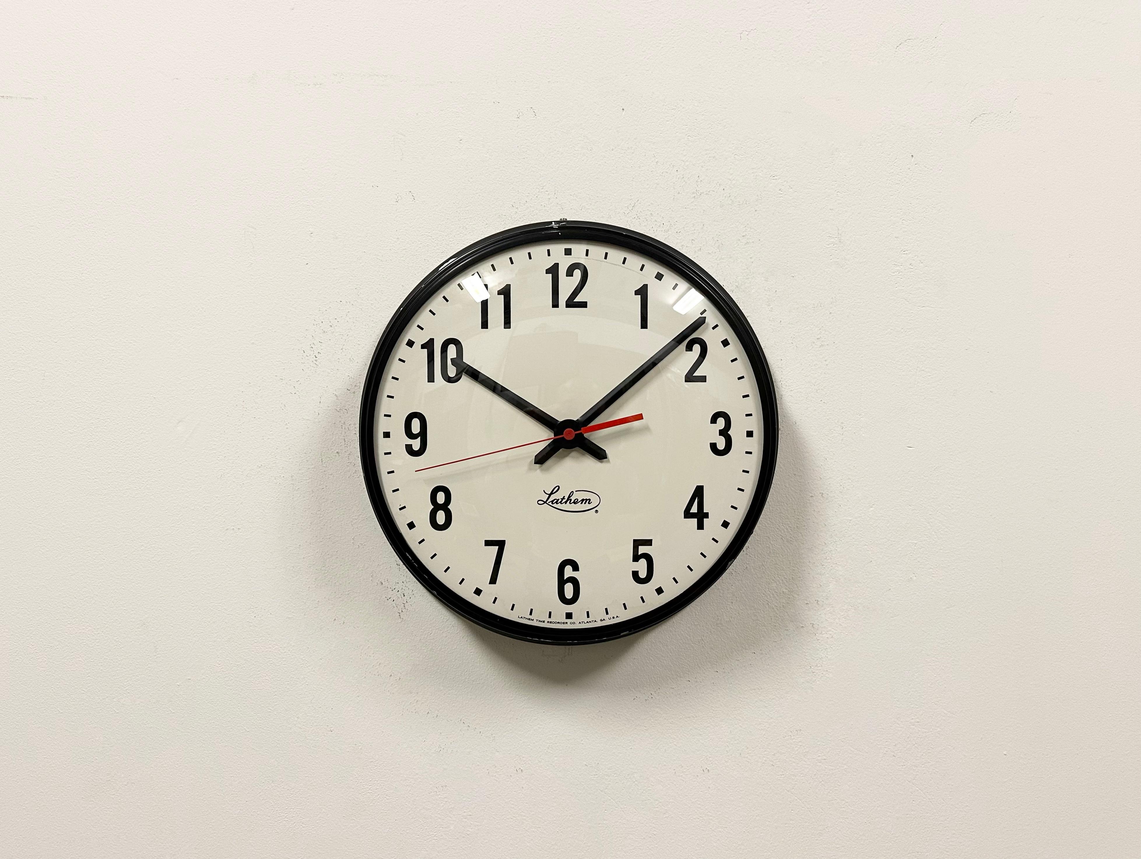 This wall clock was produced by Lathem in United states during the 1980s. It features a black metal frame, a metal dial and a convex clear glass cover. The piece has been converted into a battery-powered clockwork and requires only one AA-battery.