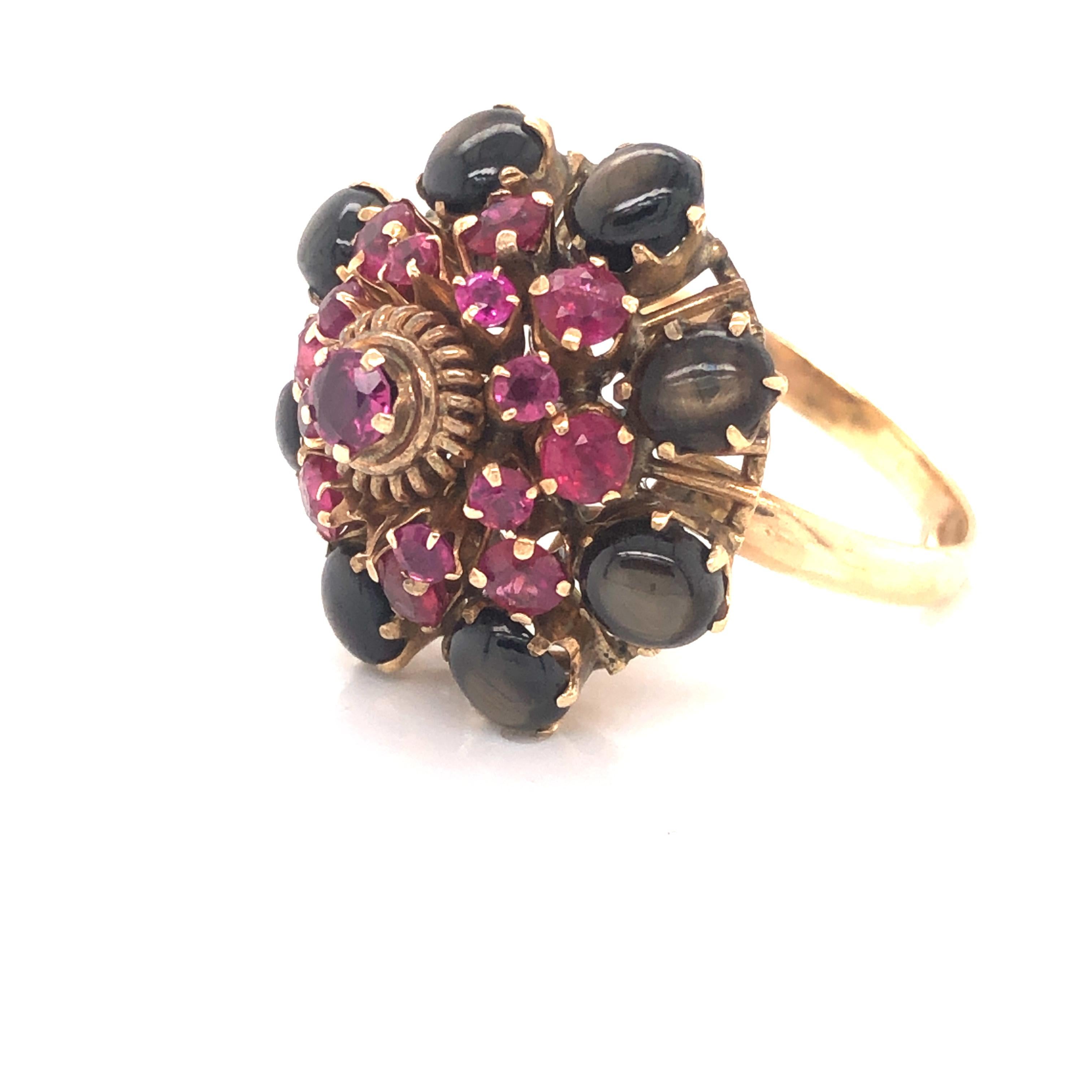 Fantastic design on this vintage 18k yellow gold ring. The ring is highlighted with natural black star sapphire and ruby gemstones. The base of the design is set with eight black star sapphire cabochon gemstones.  All gemstones show a sharp star