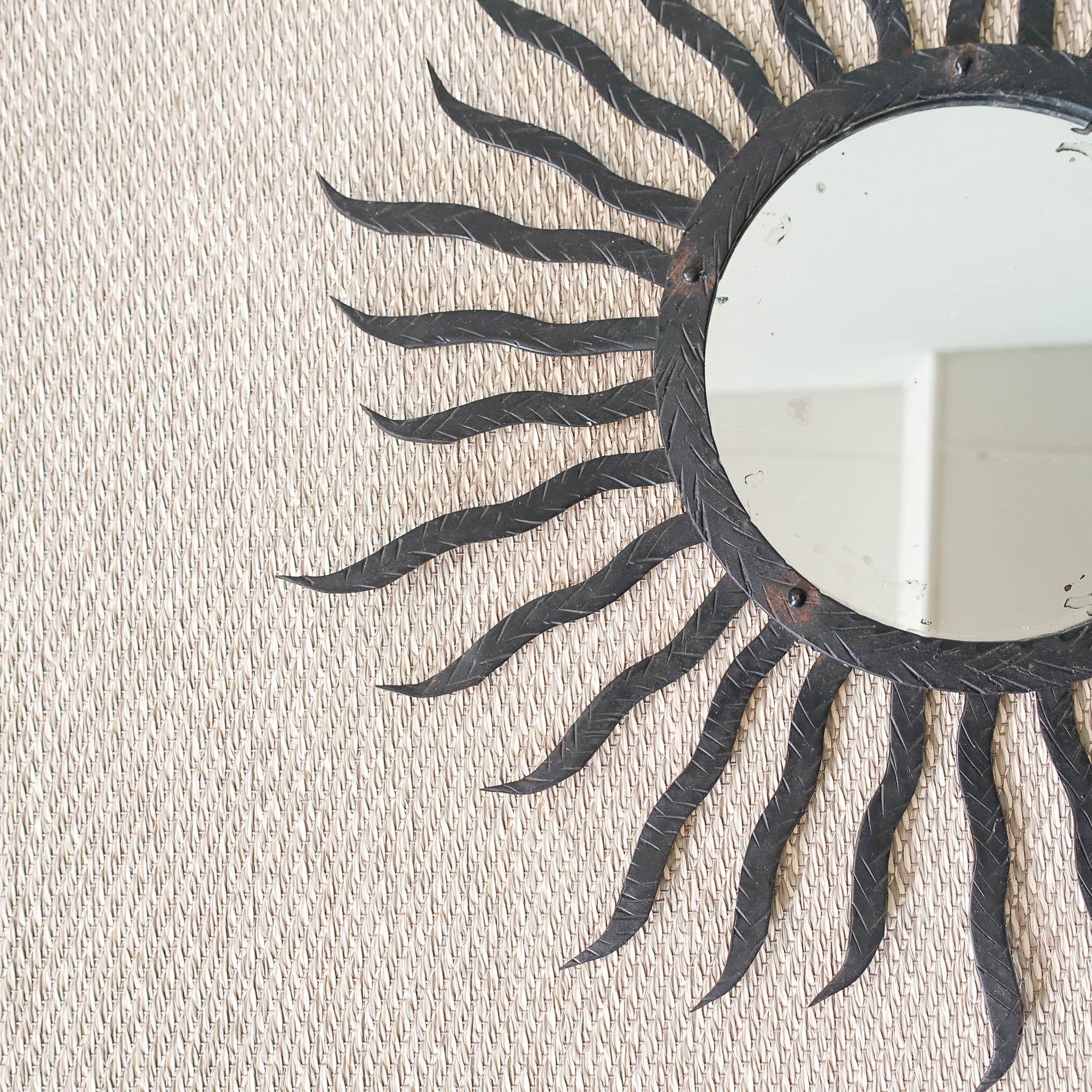 This sunburst mirror was designed and produced in Italy, during the 1950’s.
It features a carved black metal frame made of long and shorter ones. The ring surrounding the central mirror has also a carved decorative random pattern. 
In original and