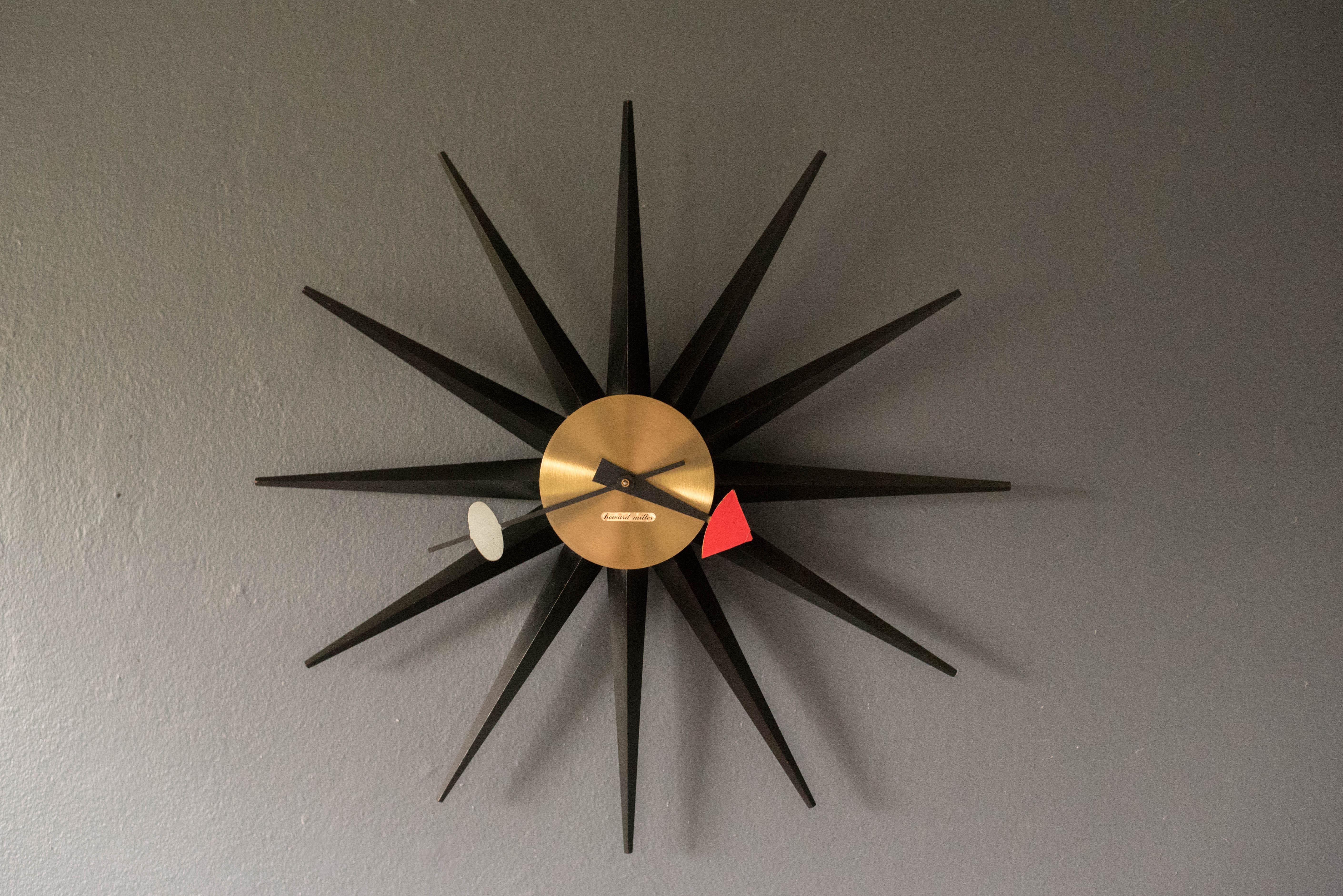 Classic Mid Century Modern sunburst wall clock designed by George Nelson for Howard Miller Clock Company, circa 1950's. This iconic piece is all original made with black lacquered wood spikes and a brass face. Keeps time with a plug in electric