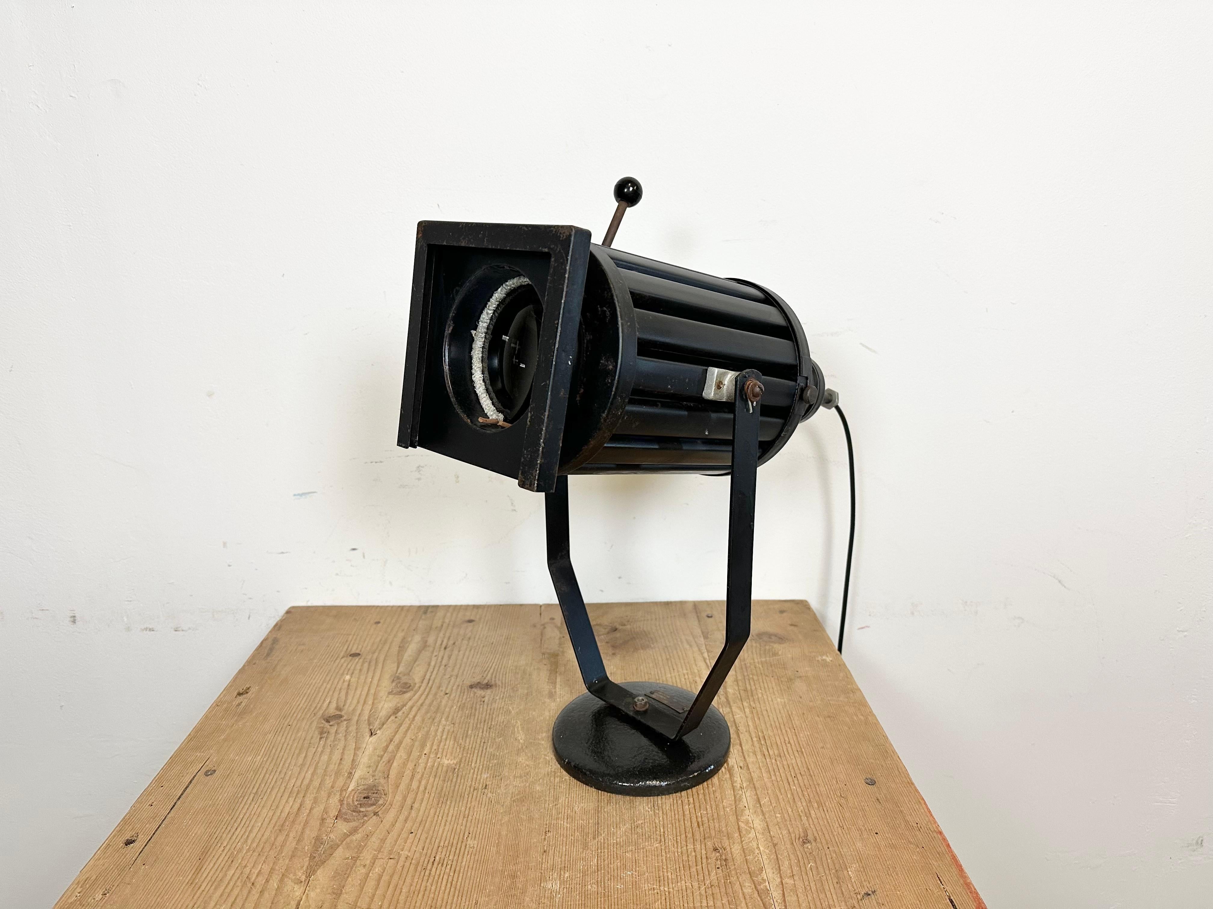 - Lámpara de mesa vintage con foco de teatro fabricada en la antigua Checoslovaquia en los años 60 
- Tiene un cuerpo de metal negro, una base de hierro fundido y una cubierta de cristal transparente para la lente
- El casquillo de porcelana