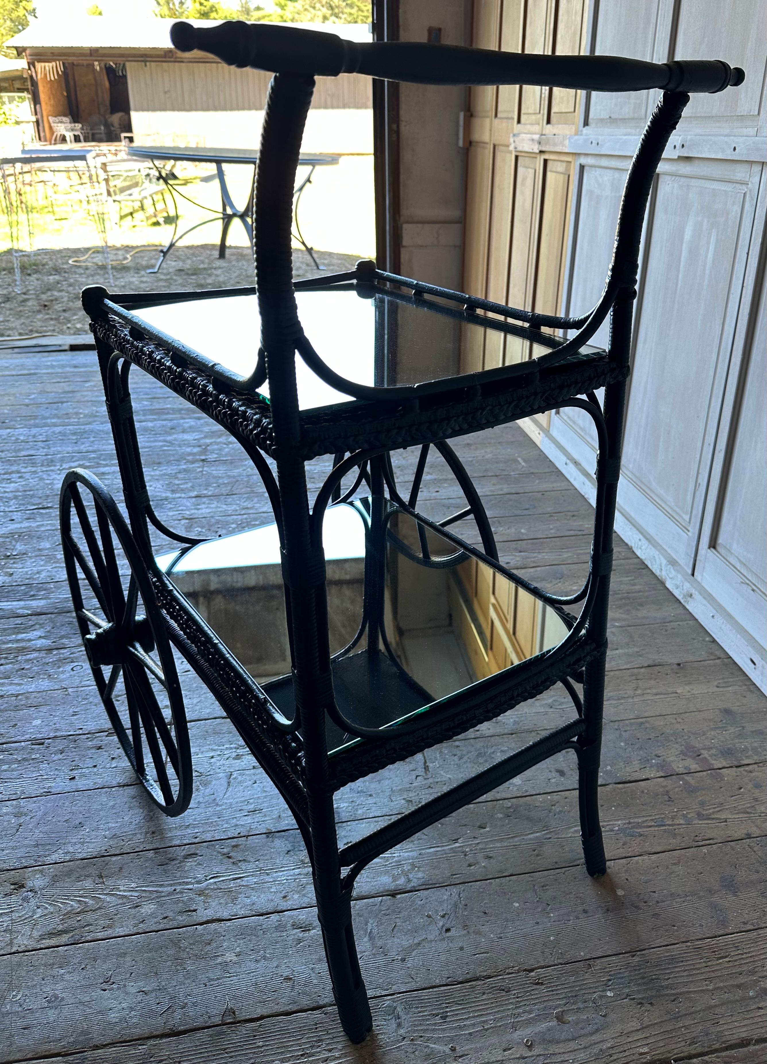 Fine vintage wicker cottage style tea, wine liquor or drinks serving cart with black painted woven rattan/wicker and bentwood gallery around the top and lower mirrored shelves. The upper tier with sides.  A tall wood handle on one end and two large