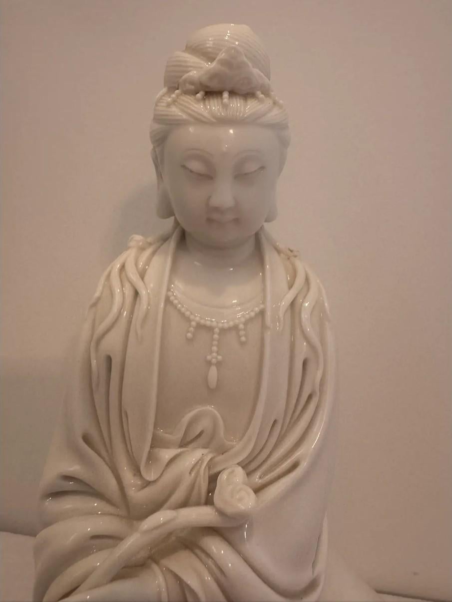 Una serena figura vintage in porcellana Blanc de Chine di Guanyin, la dea buddista della misericordia e della compassione. Realizzata in luminosa porcellana bianca, la dea è raffigurata seduta in abiti fluenti, adornata con gioielli di perline e con