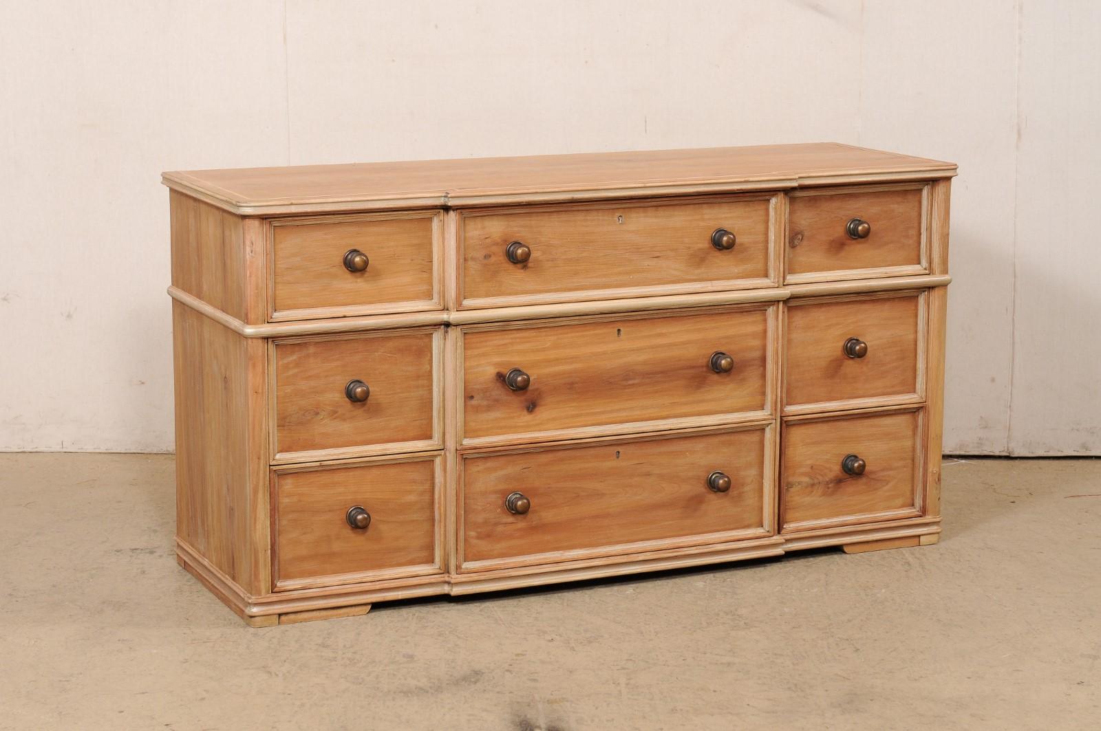 A vintage American bleached wood chest of nice drawers. This larger-sized case has a shallow break-front design, and features a case that houses nine drawers total, made up of three horizontal rows; each row having a pair of smaller end-drawers