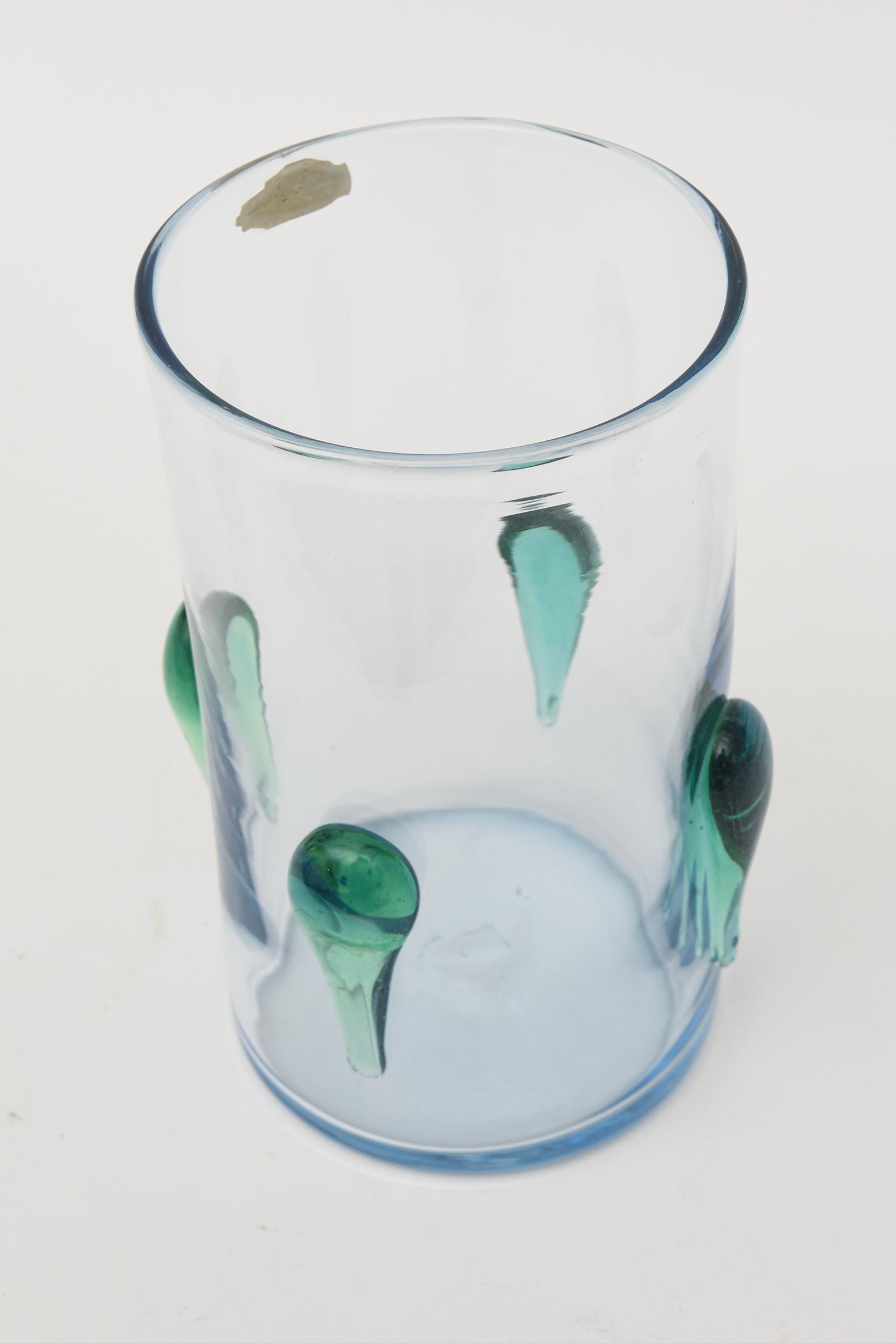 This vintage Blenko glass vase from the 60's has the original paper sticker on it from the time period. The clear glass cylinder vase has 4 applied dimensional teardrop forms surround. The colors are a combination sea green infused with a light