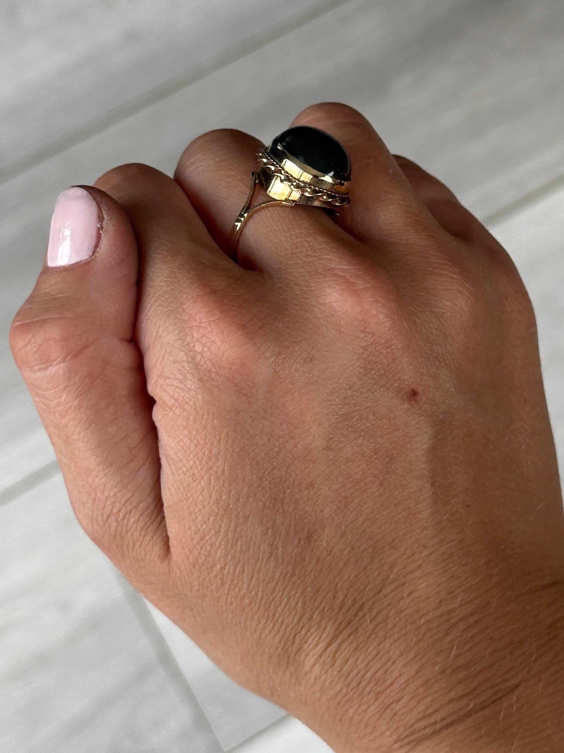 La brillante y lisa piedra de sangre de este anillo está engastada de forma sencilla, pero el engaste tiene un marco detallado de torsión de cuerda que luego desciende hasta los hombros divididos. Fabricado en Birmingham, Inglaterra. 

Tamaño del